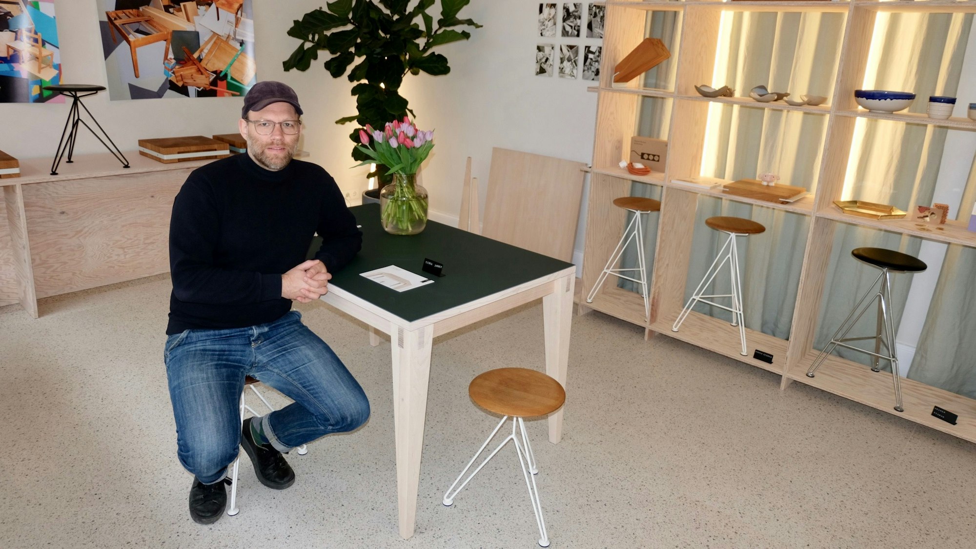 Gunnar Brand am Tisch „Joseph“ mit Hockern „Sisman“ in dem Ladenlokal der Möbel Compagnie.