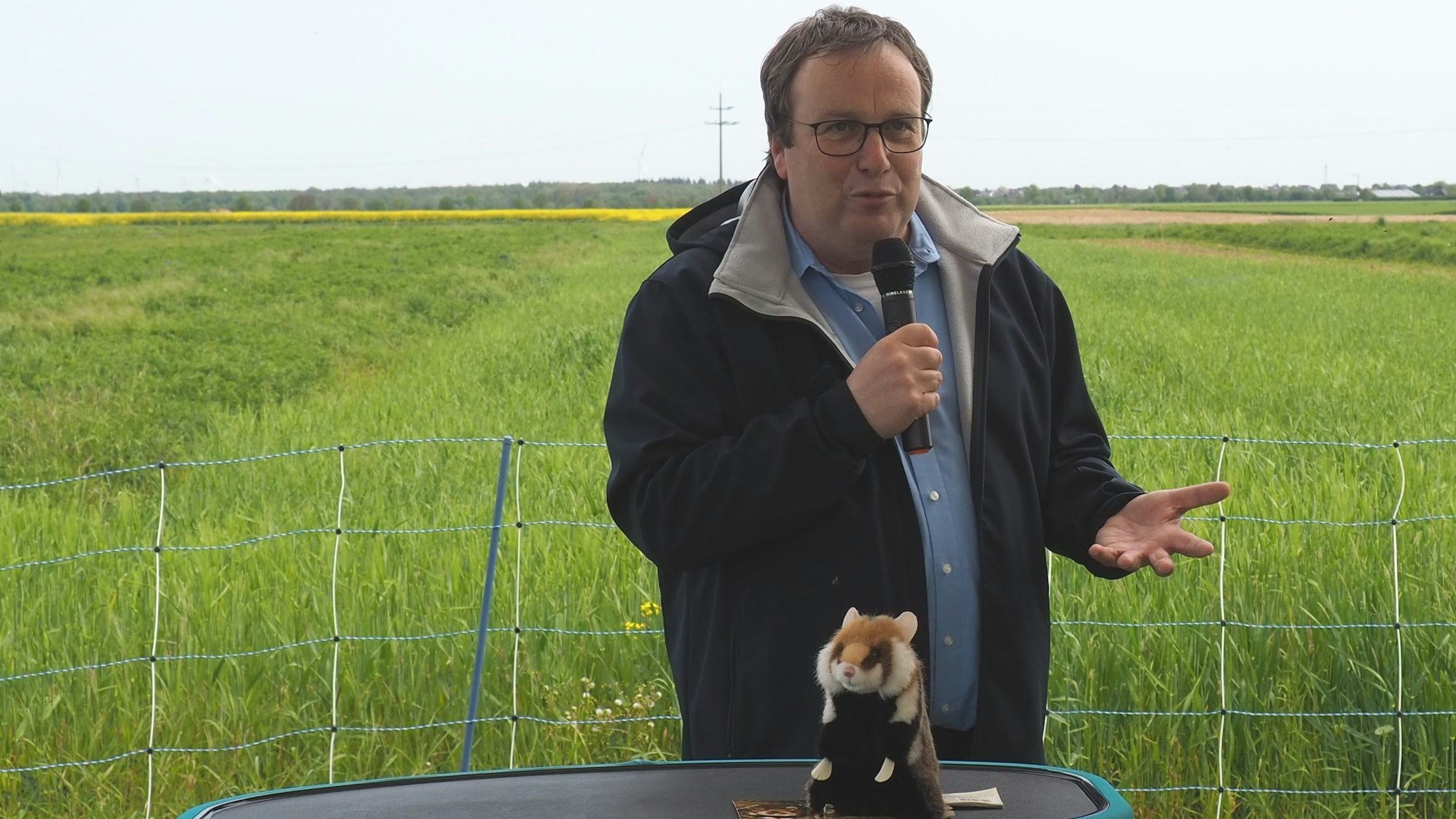 Minister Oliver Krischer spricht in ein Mikrofon. Vor ihm steht ein Plüschhamster.