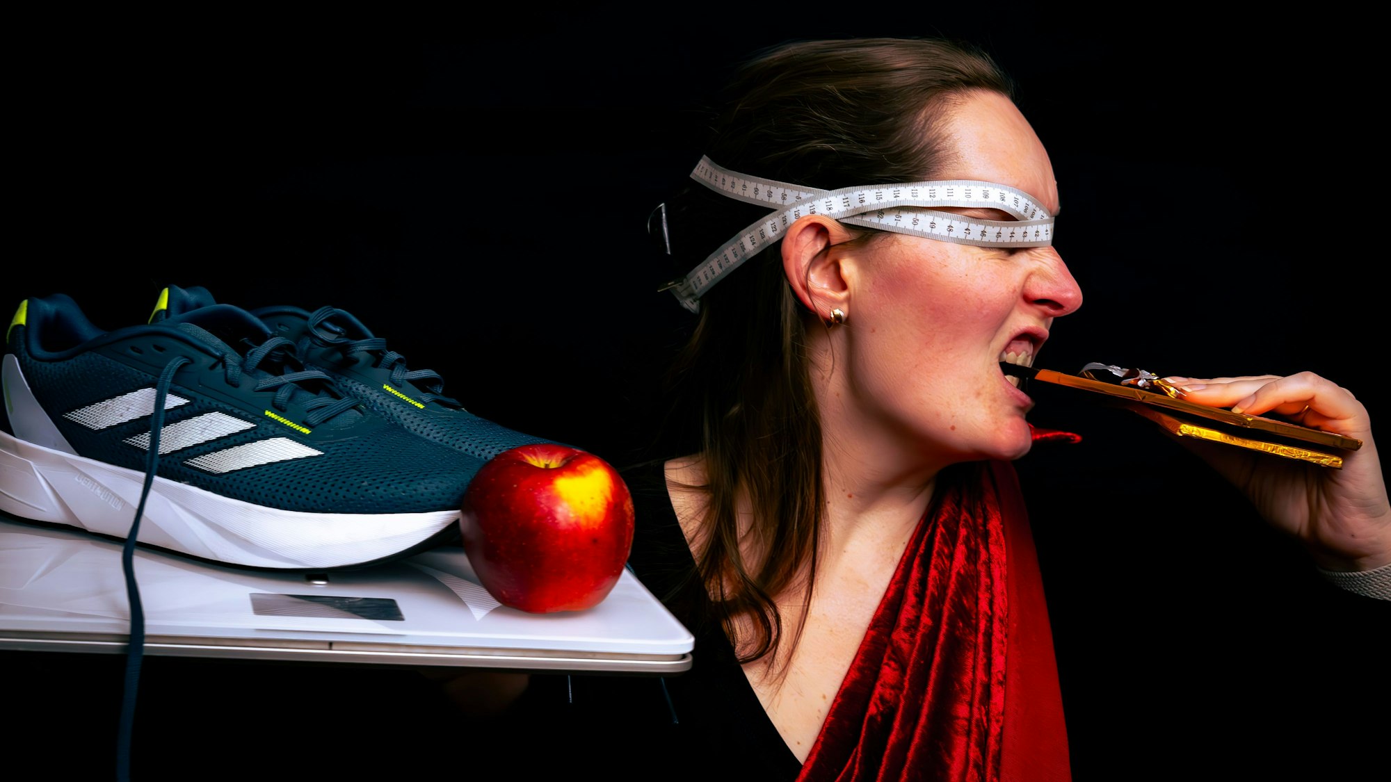 Christina Roggendorf beißt in eine Tafel Schokolade, ein Maßband verschließt ihr die Augen. In der anderen Hand hält sie Waage, Apfel und Sportschuhe.