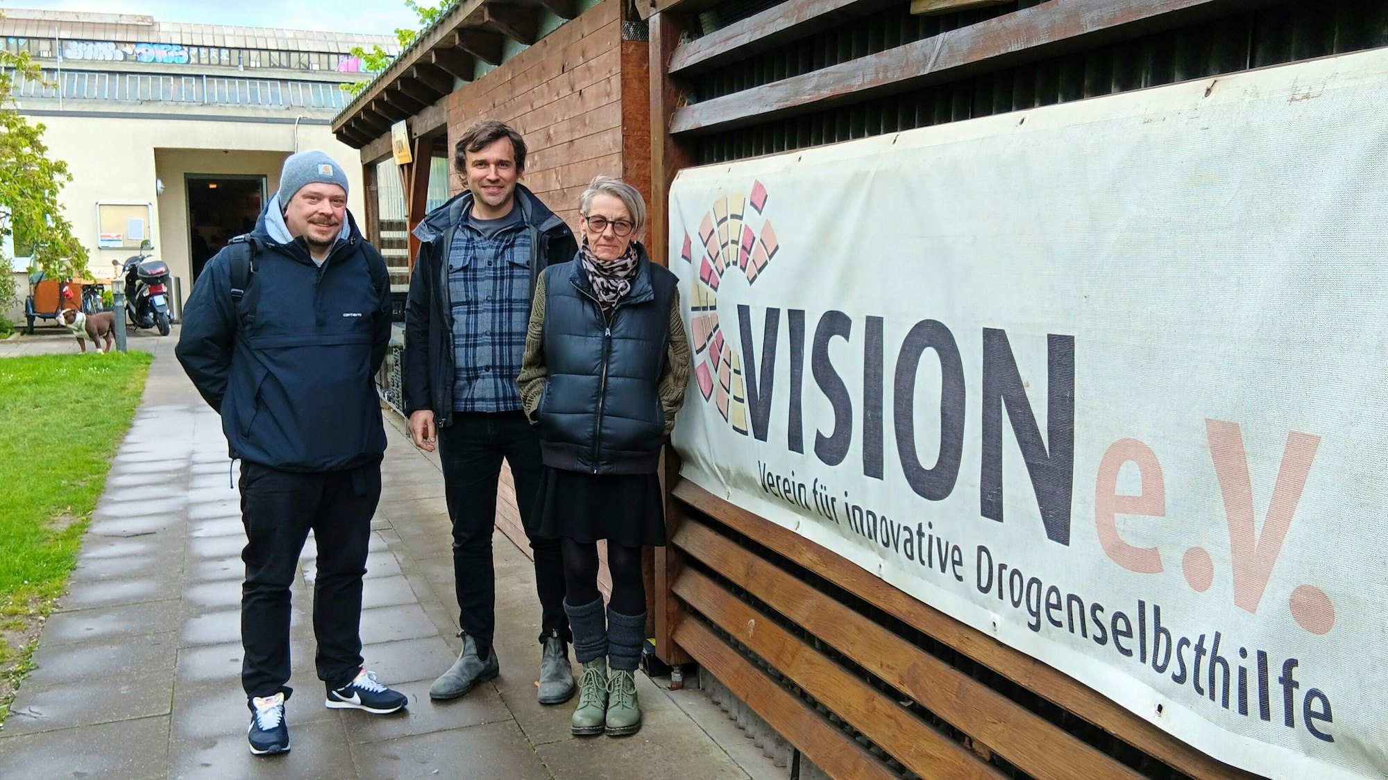 Drei Personen stehen vor einem Banner des Vision-Vereins.
