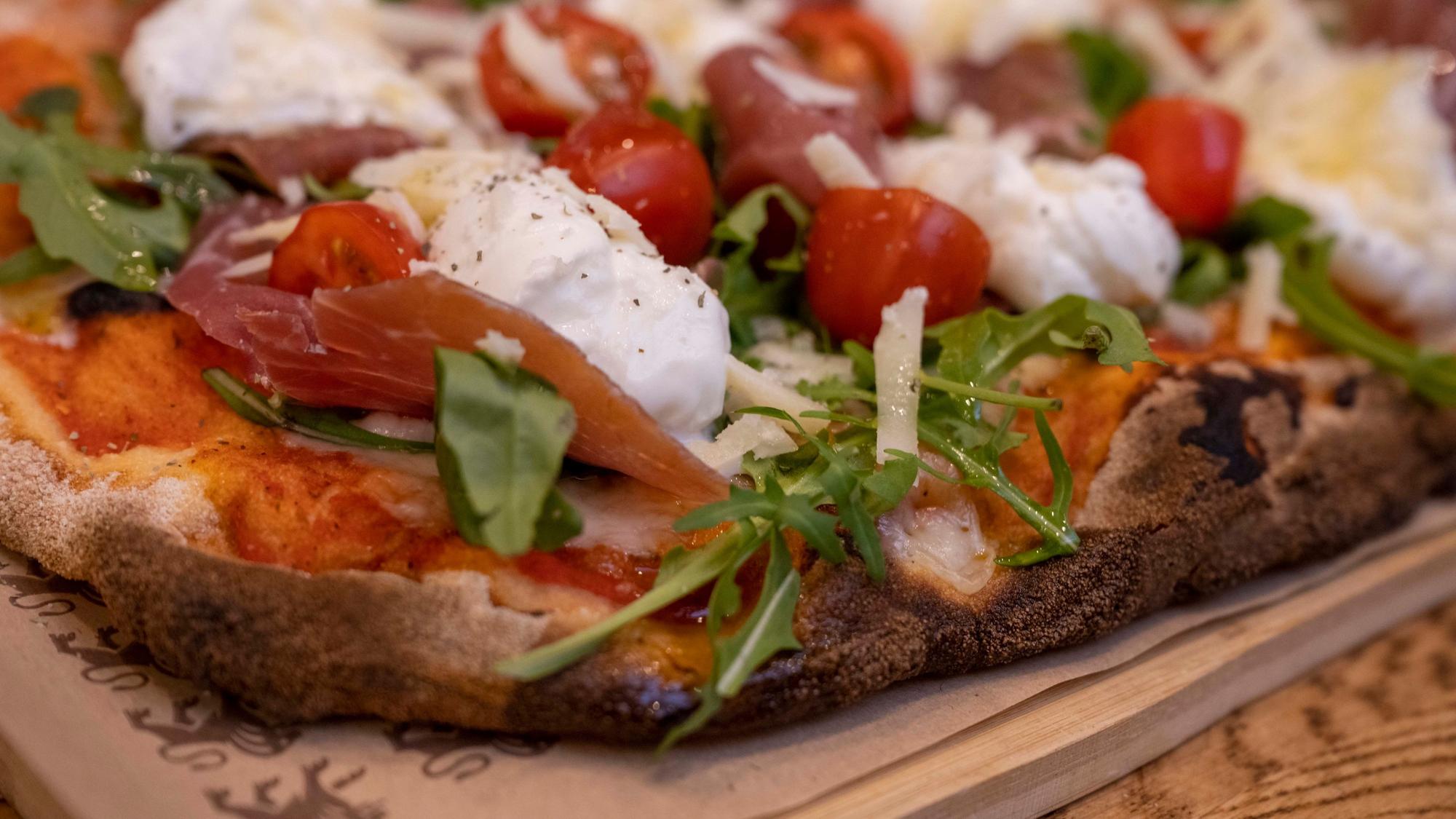 Eine fertige Pinsa, belegt unter anderem mit Tomaten, Rucola und Büffelmozzarella.
