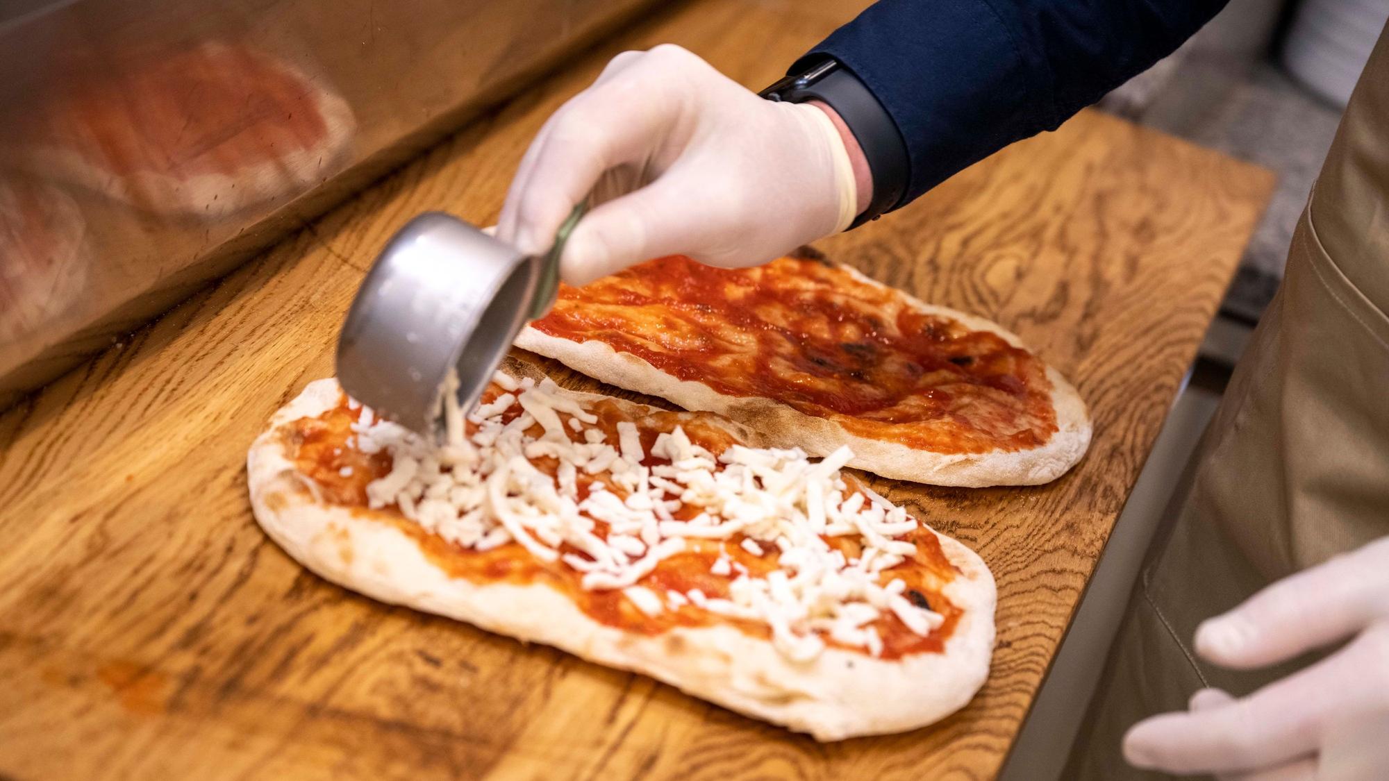 Die Pinsa wird mit Tomatensoße bestrichen und mit geriebenem Mozzarella belegt. Danach kommt sie in den Ofen.