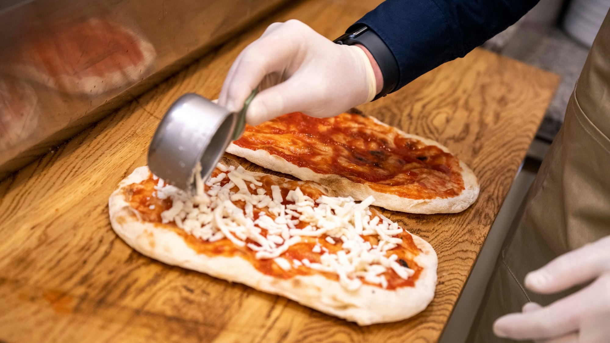Die Pinsa wird mit Tomatensoße bestrichen und mit geriebenem Mozzarella belegt. Danach kommt sie in den Ofen.