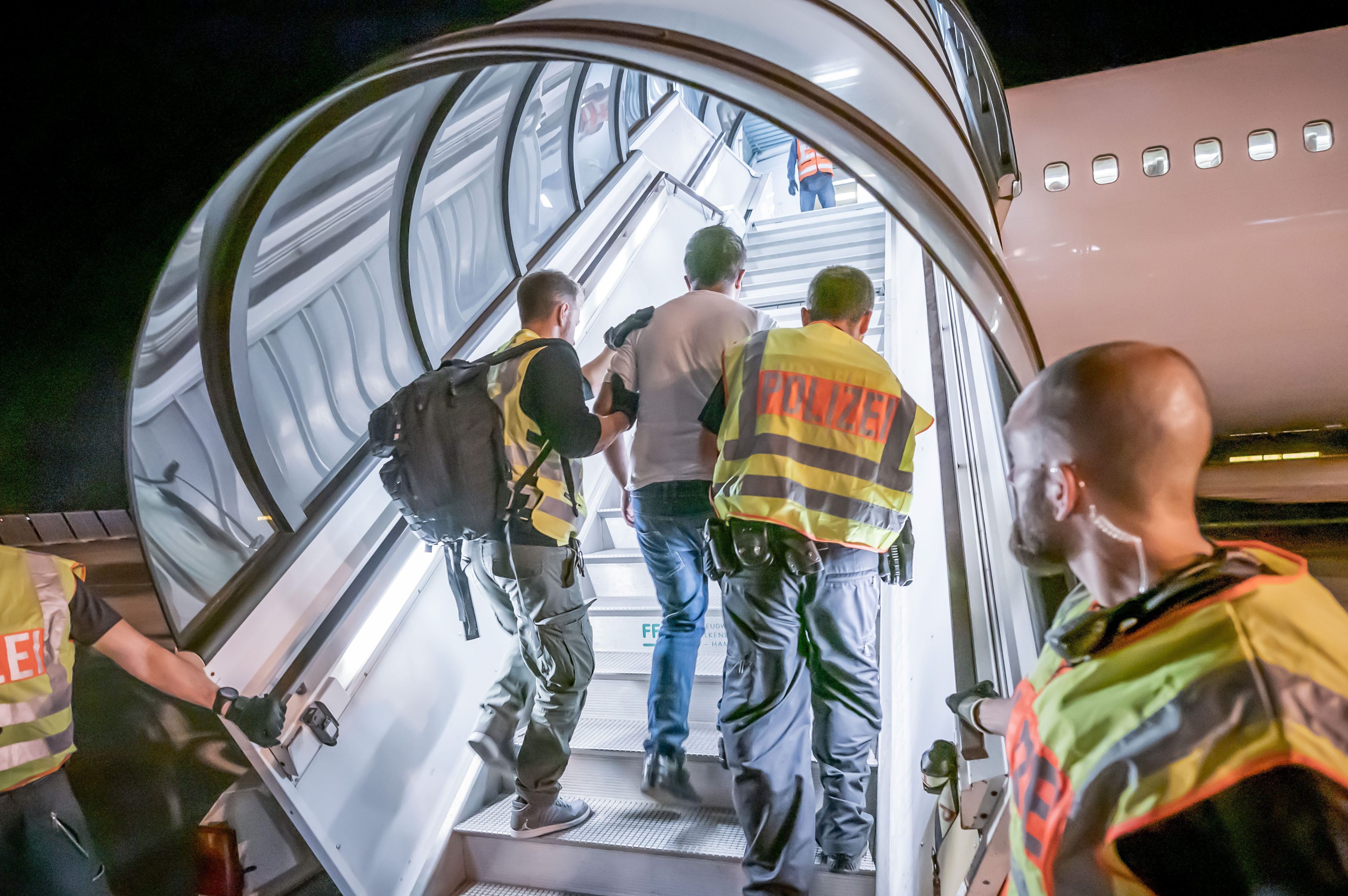 Polizeibeamte begleiten einen Mann auf einem in ein Charterflugzeug.