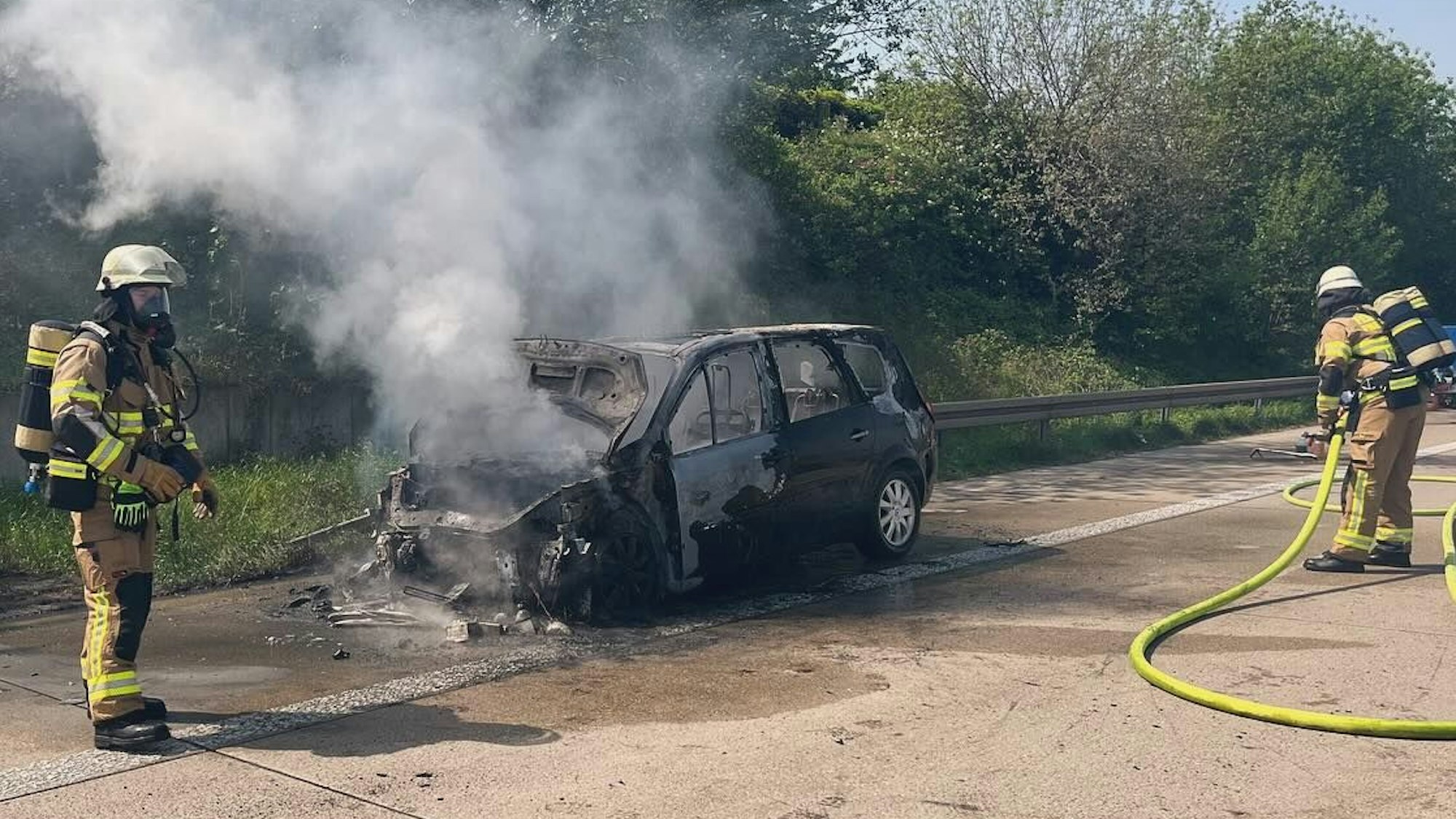Zwei Feuerwehrleute löschen den brennenden Wagen auf der A4.
