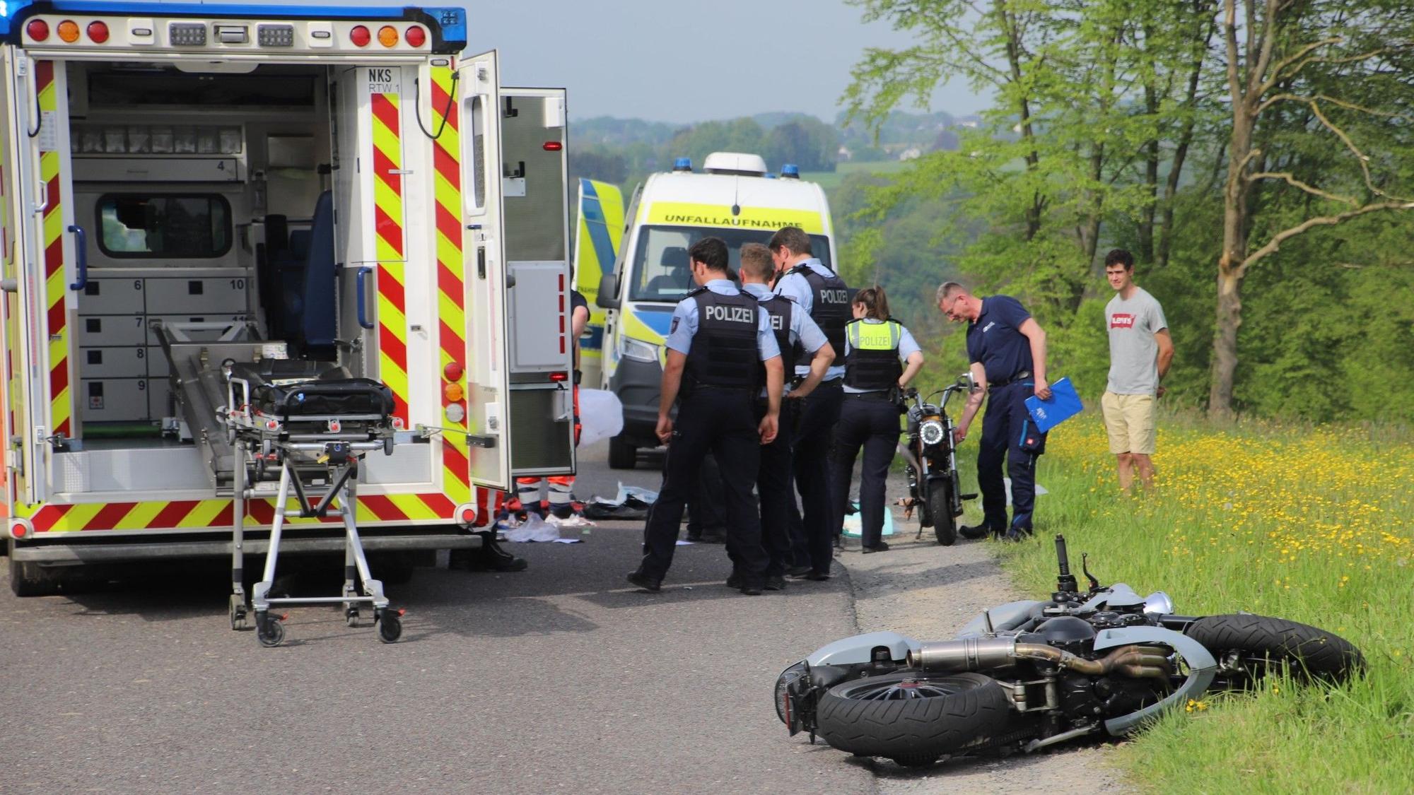 Polizisten stehen an einer Unfallstelle, ein Krankenwagen steht neben ihnen, ein Motorrad liegt auf der Straße.