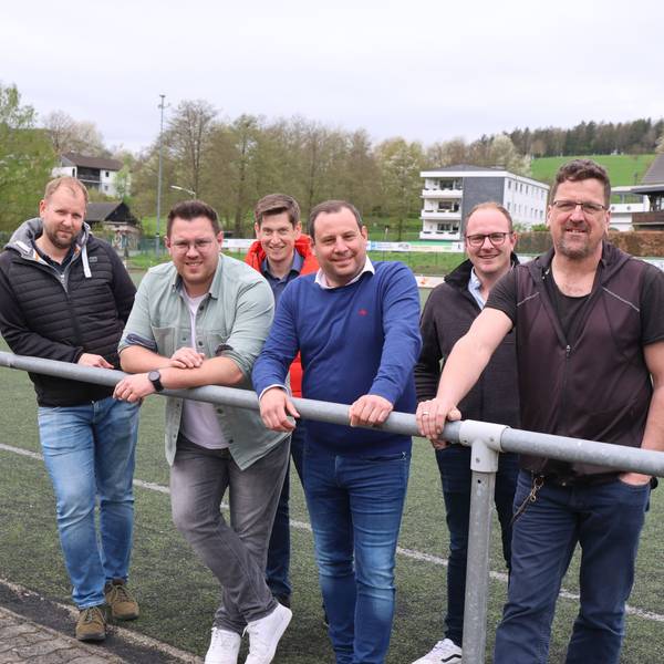 Sechs Männer stehen am Spielfeldrand des Kunstrasenplatzes.