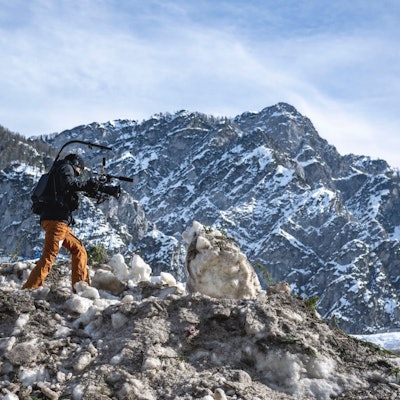 Eine Kamerafrau läuft über einen Haufen Schnee in den Bergen.