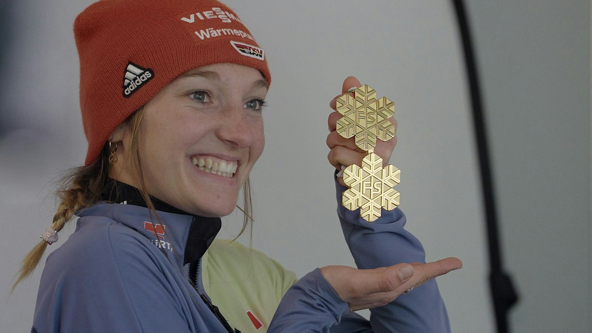 Katharina Schmid hält eine Medaille in die Luft.