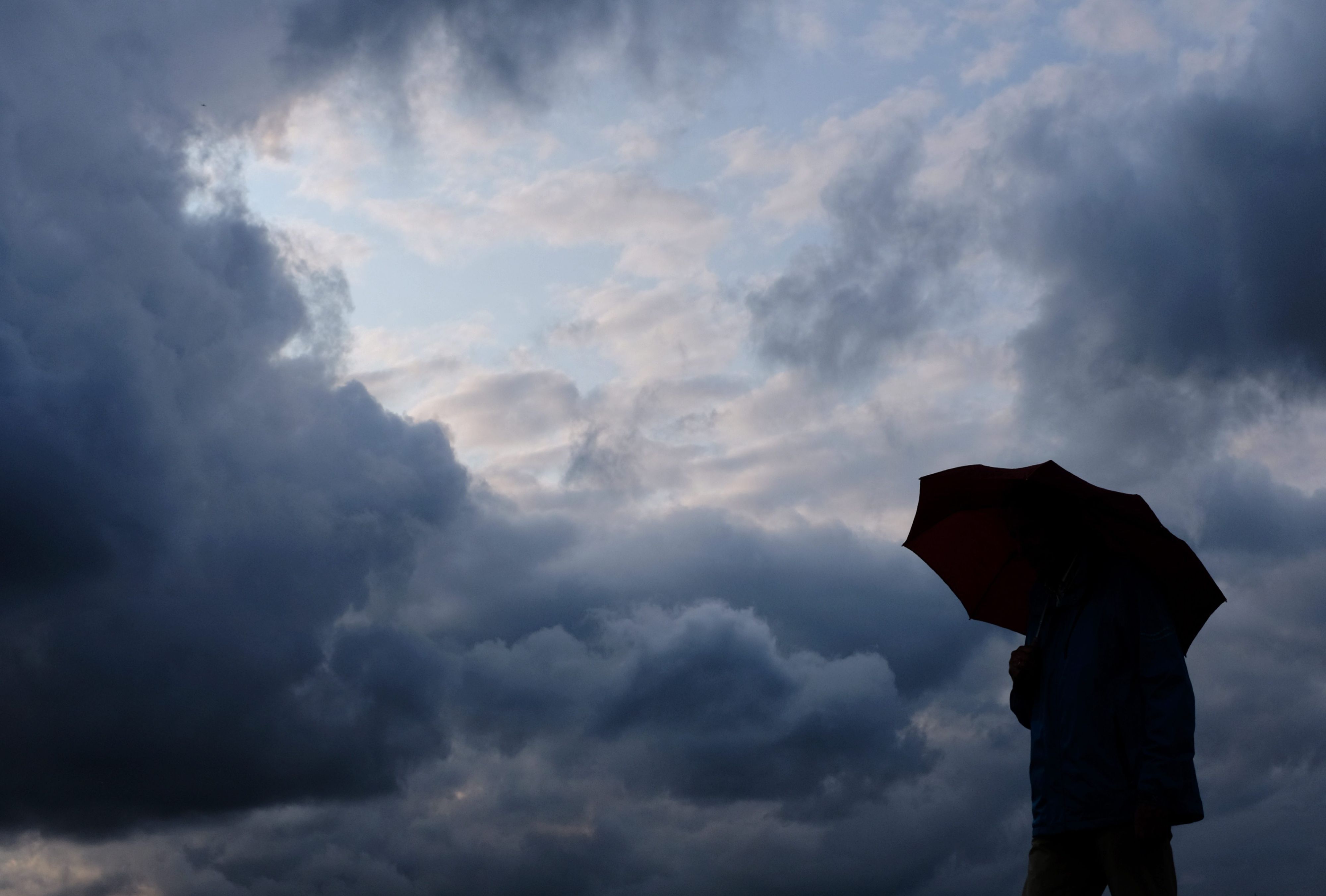Ein Mann geht mit einem Regenschirm vor aufziehenden dunklen Wolken spazieren. (Symbolfoto)