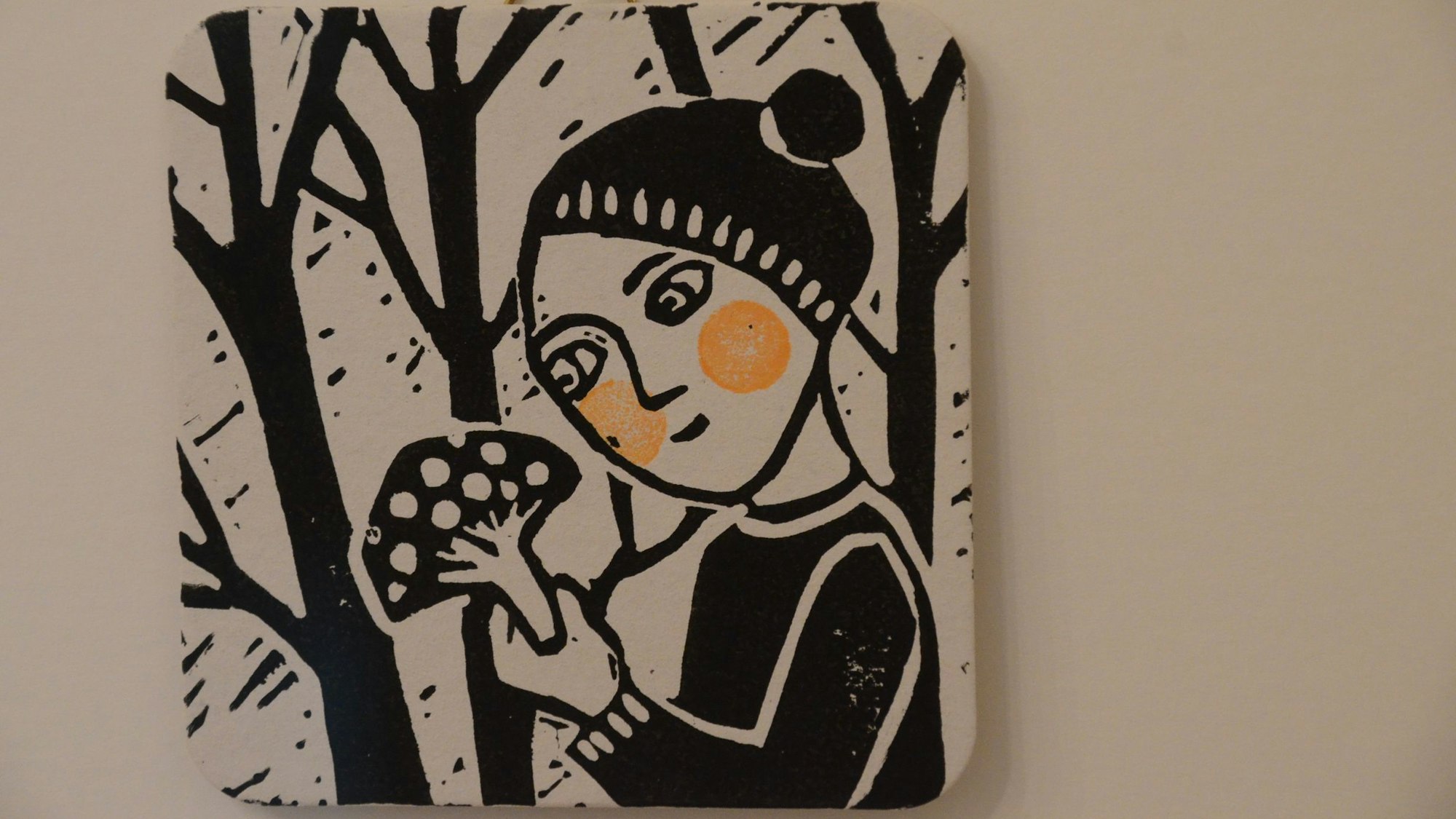 Ein Linoldruck in schwarz-weiß im quadratischen Format eines Bierdeckels. Zu sehen ist ein Mädchen, das in der Hand einen Fliegenpilz hält. Die Wangen des Kindes sind orangerot, die einzige Farbe im Bild.