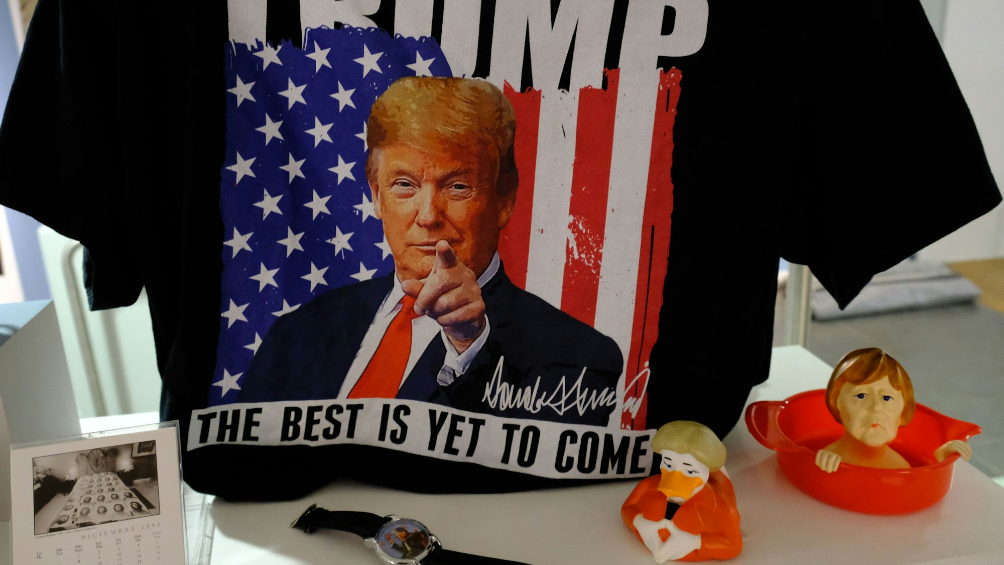 Ausstellungsstücke der Kitsch-Ausstellung: Ein Donald-Trump-T-Shirt, eine Angela-Merkel-Ente und eine Zitruspresse mit dem Konterfei der Ex-Kanzlerin.