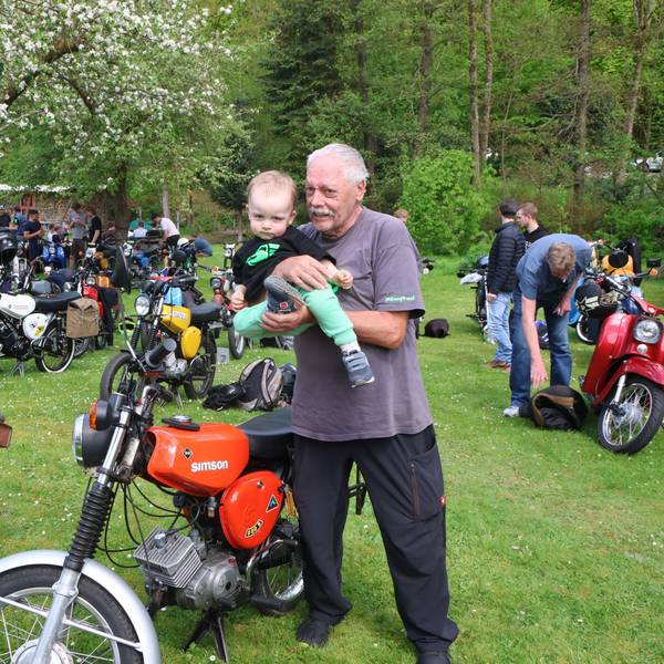 Ein älterer Herr zeigt einem kleinen Kind ein Motorrad.