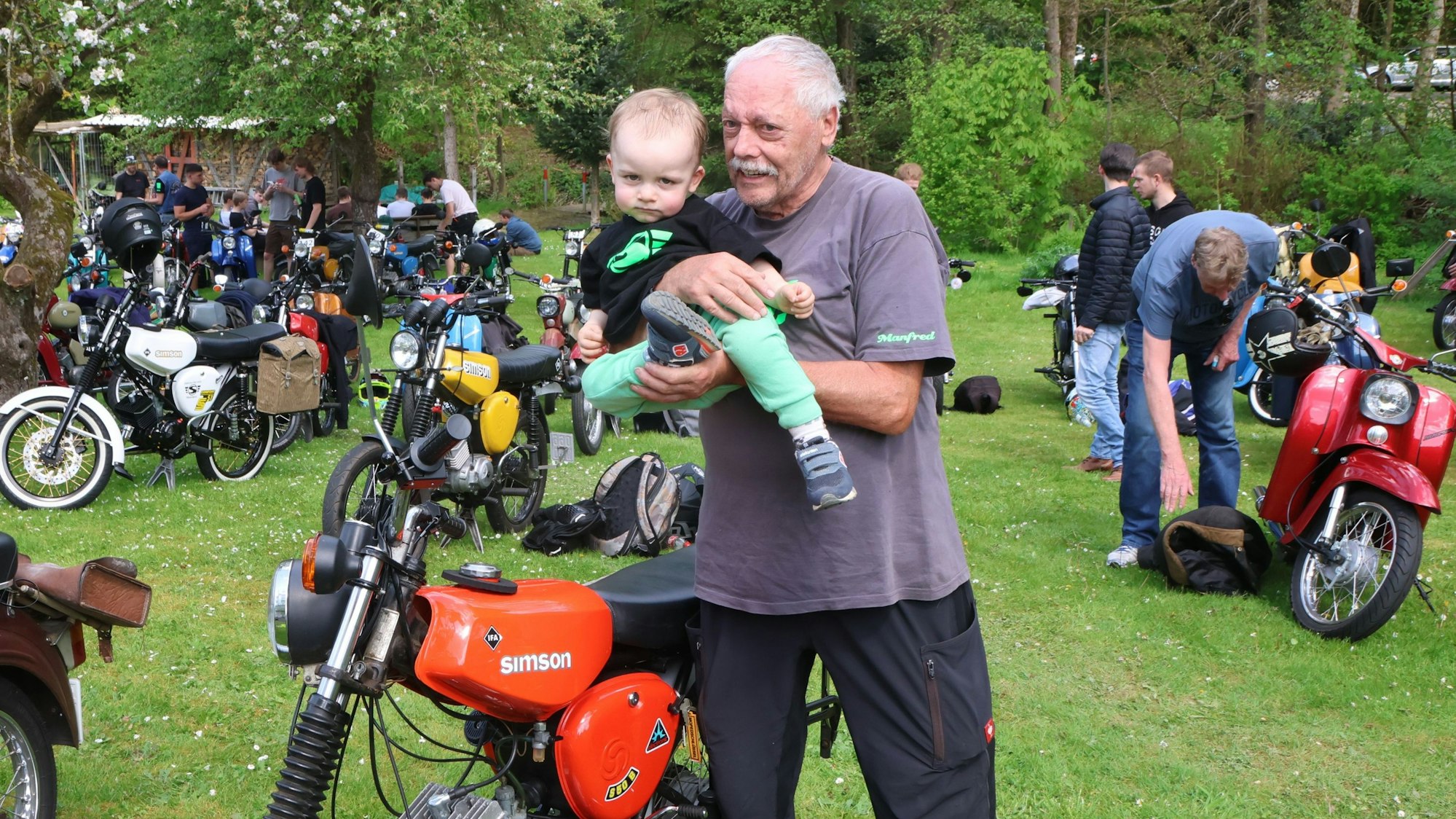 Ein älterer Herr zeigt einem kleinen Kind ein Motorrad.