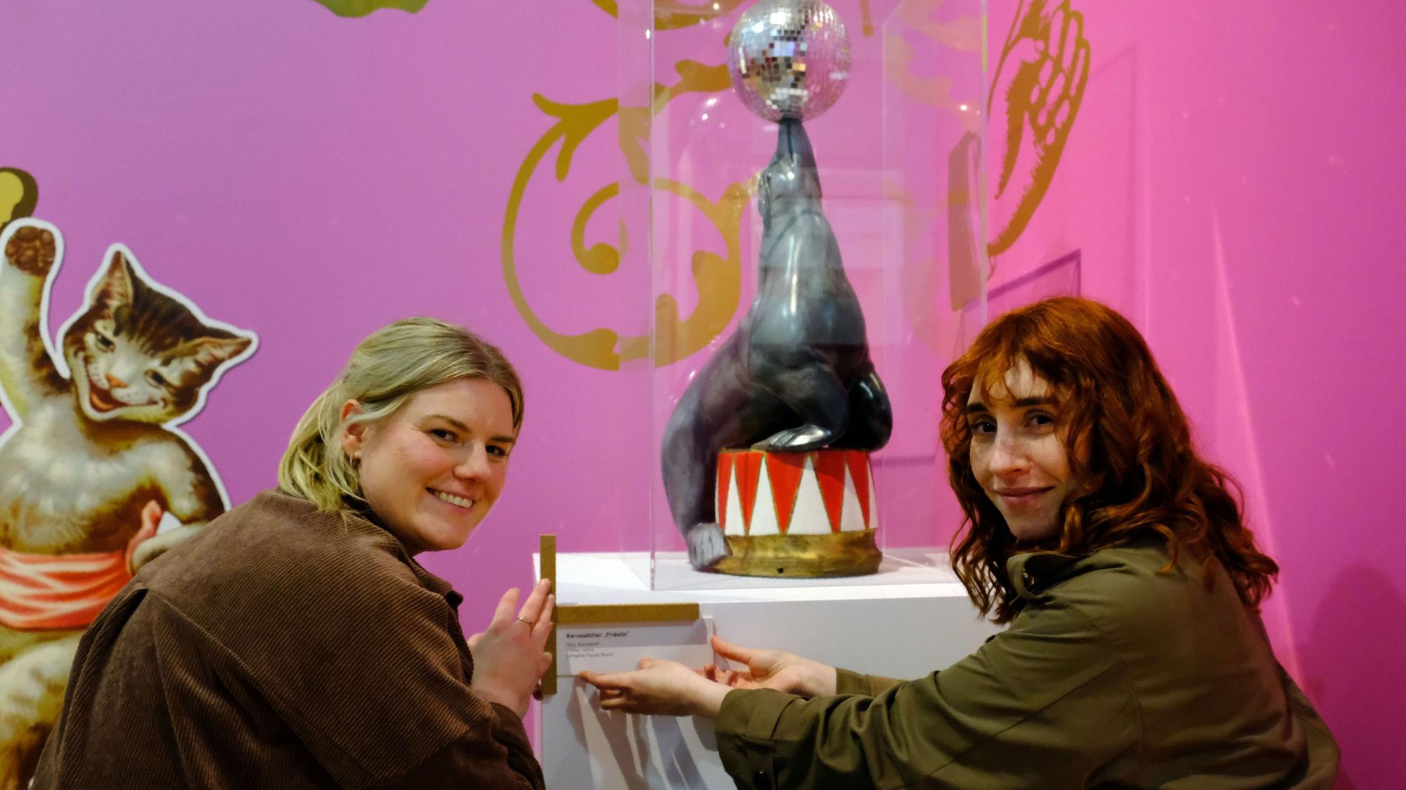 Kuratorin Ann Heinen (l.) und Alina Hilbrecht bringen die Beschriftung an einem Ausstellungsexponat an.