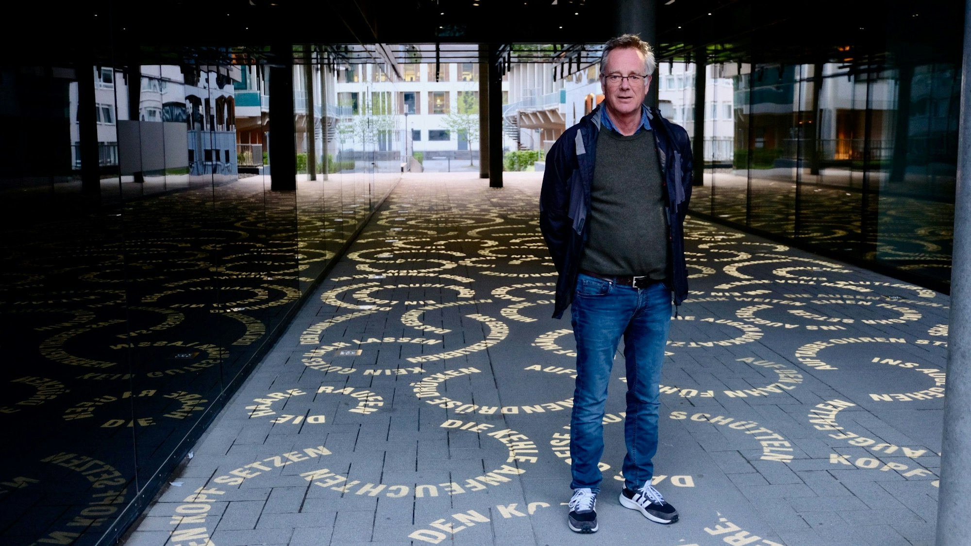 Detlef Hartung steht inmitten seiner Lichtinstallation „Körpersprache“ im Durchgang des Trio-Gebäudes der Uniklinik an der Robert-Koch-Straße. Helle, auf den Boden projizierte Kreise zeigen deutsche Redewendungen, die mit Körperteilen zu tun haben. Foto von Susanne Esch