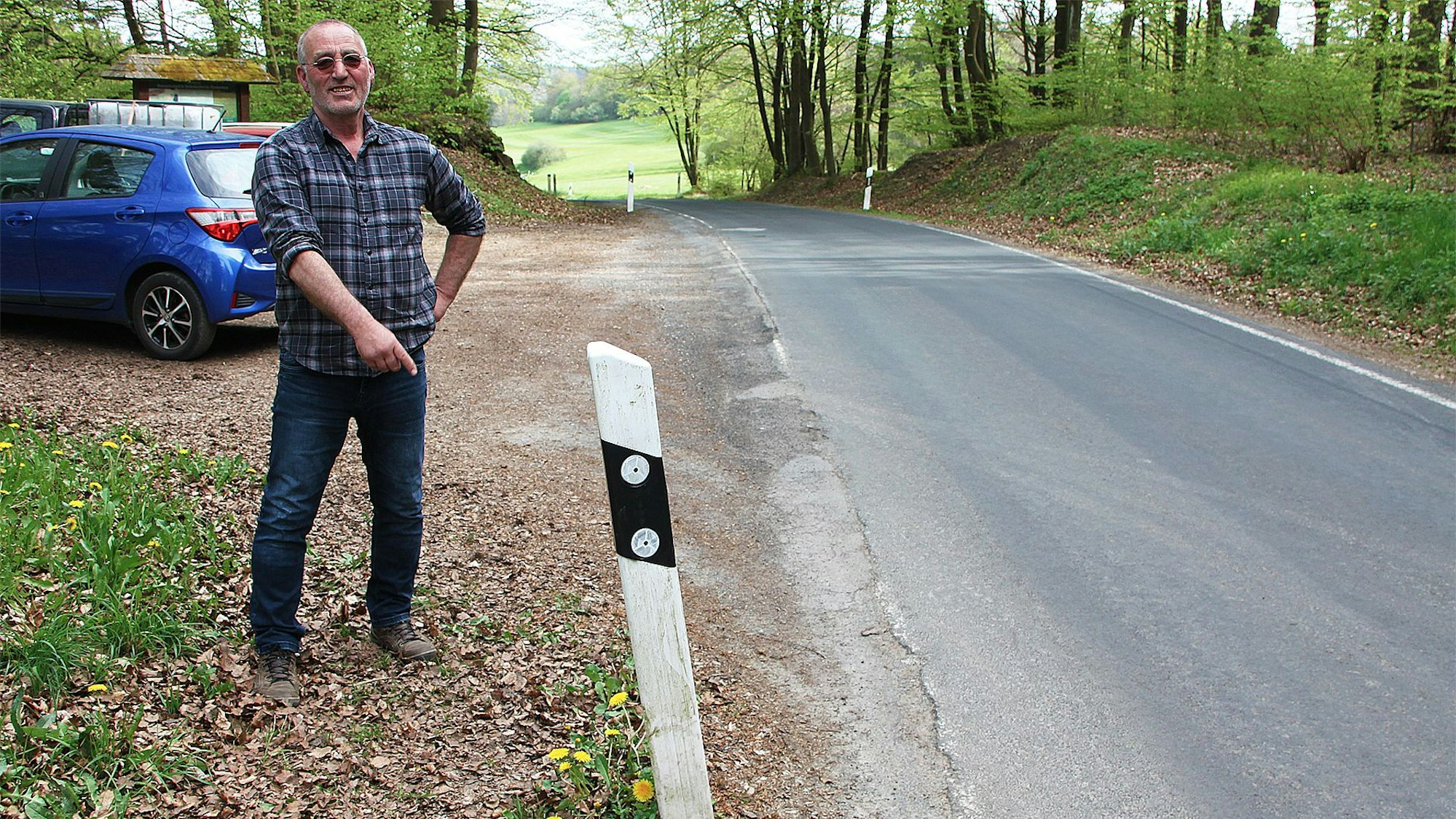 Ein Mann steht an einem Leitpfosten an einer Straße.