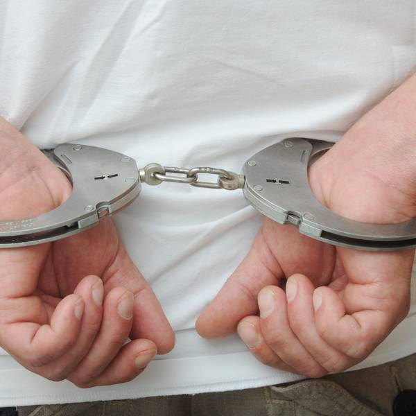 Zwei männliche Hände sind in Polizeihandschellen gefesselt.