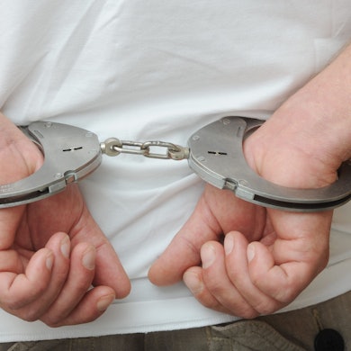 Zwei männliche Hände sind in Polizeihandschellen gefesselt.