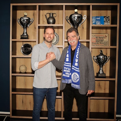 Heiner Brand und Geschäftsführer Christoph Schindler stehen vor dem Trophäenschrank des VfL Gummersbach.