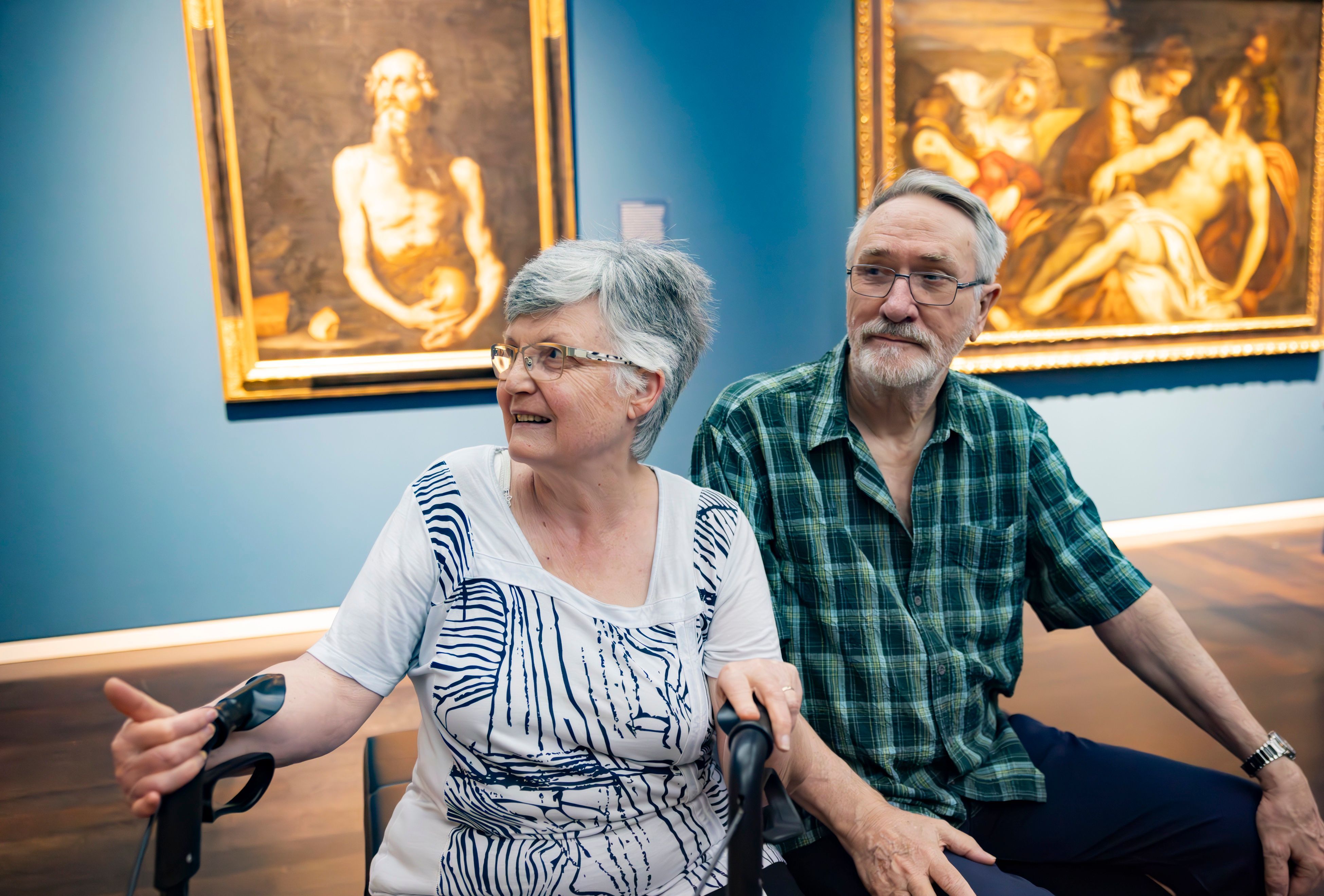 Ein älteres Paar sitzt vor einigen Kunstwerken im Museum.