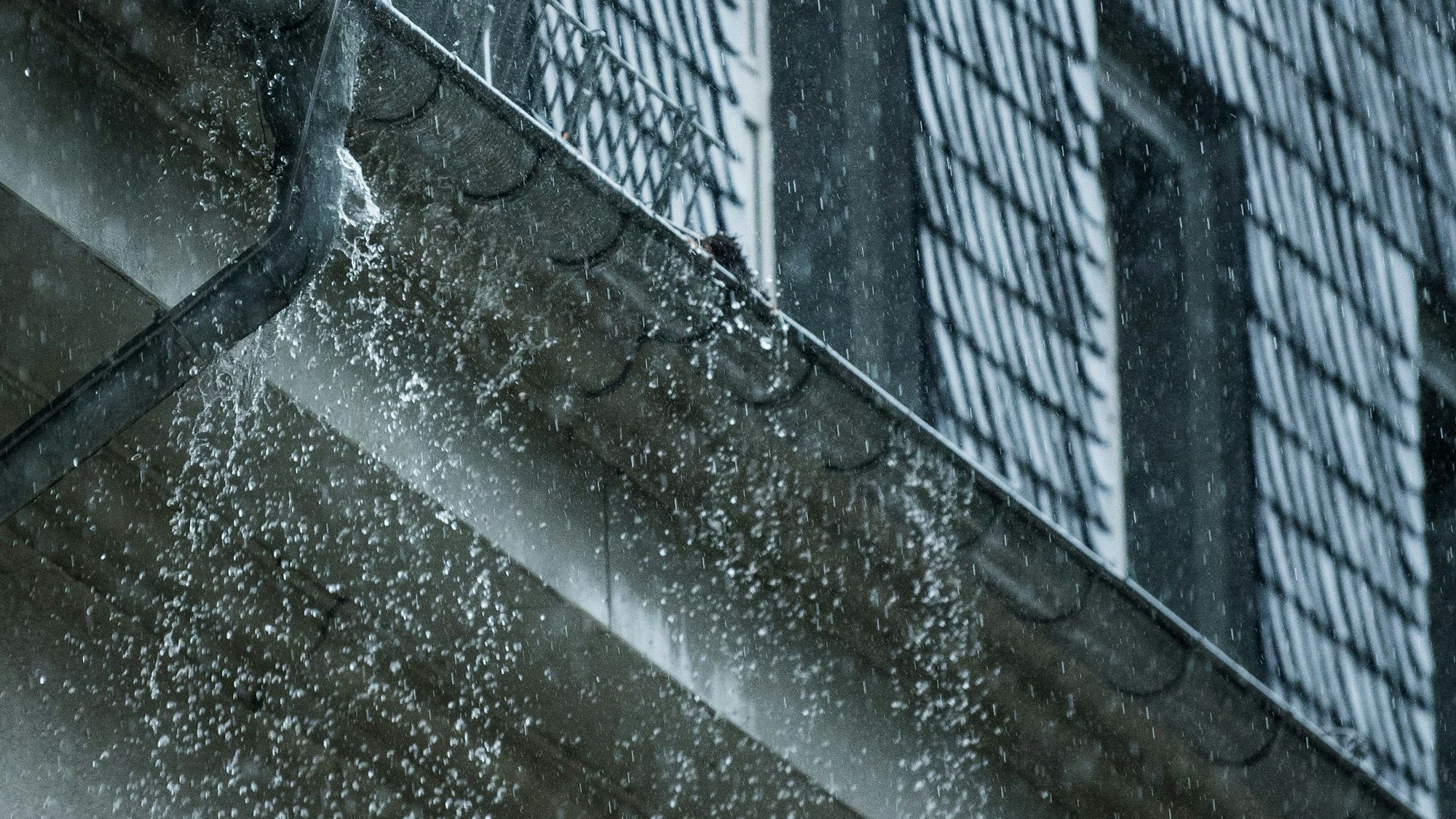 Viel Wasser fällt aus einer Regenrinne an einem Haus