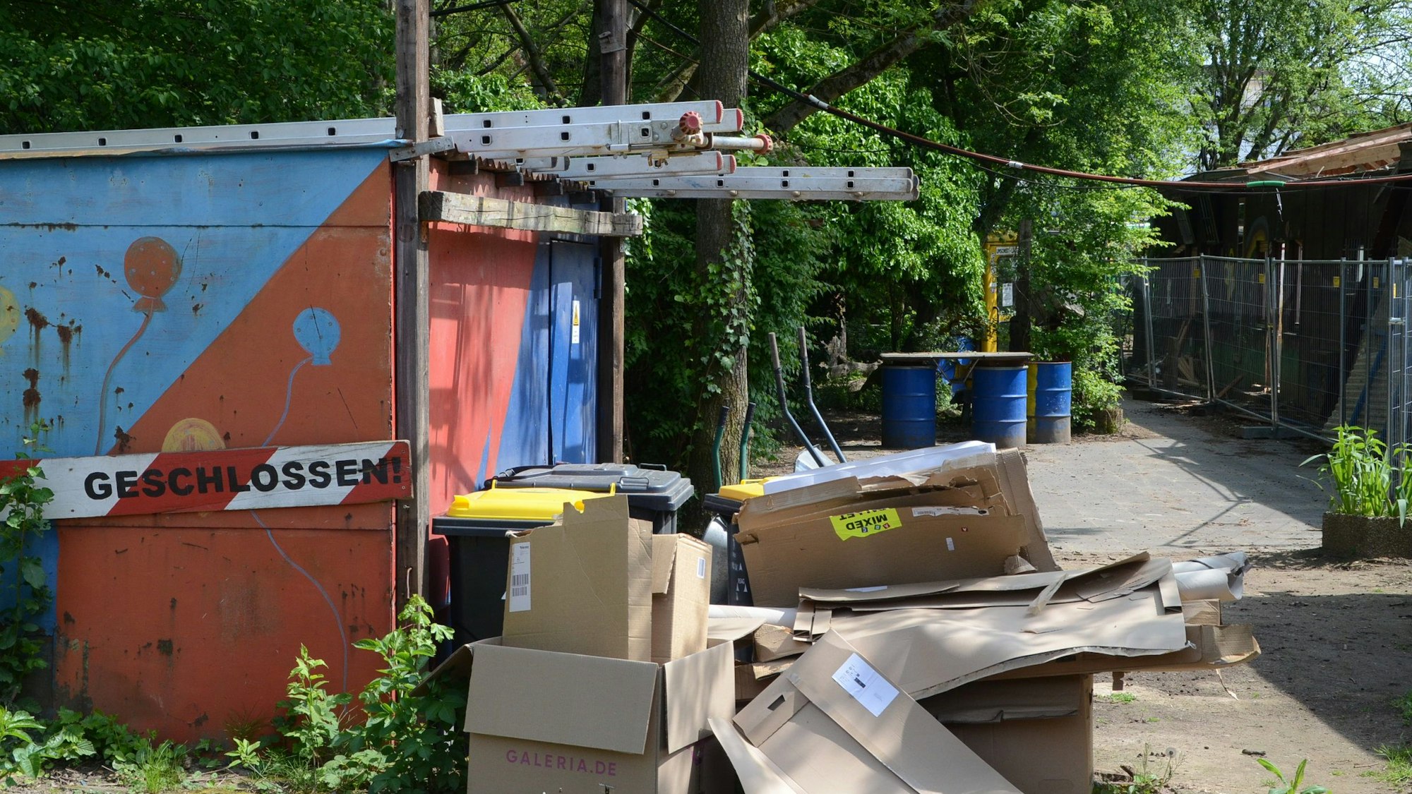 Eine bunt angemalte Metallgarage; daneben liegen Kartons.