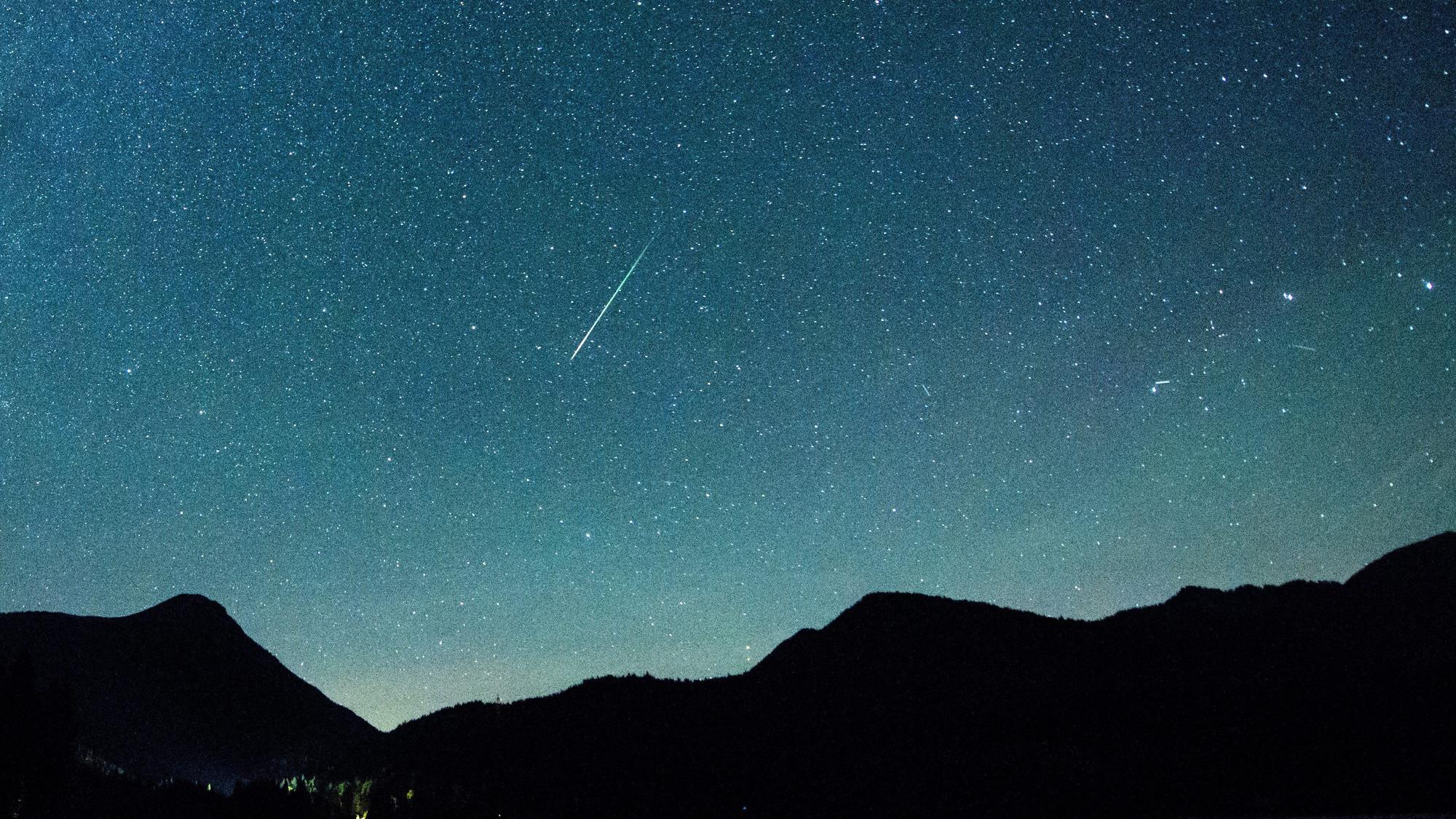 Eine Sternschnuppe leuchtet neben der Milchstraße am Himmel über dem Walchensee.