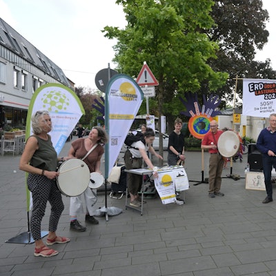 Mitglieder der Initiativen stehen vor Plakaten und trommeln, um auf ihre Veranstaltung aufmerksam zu machen.