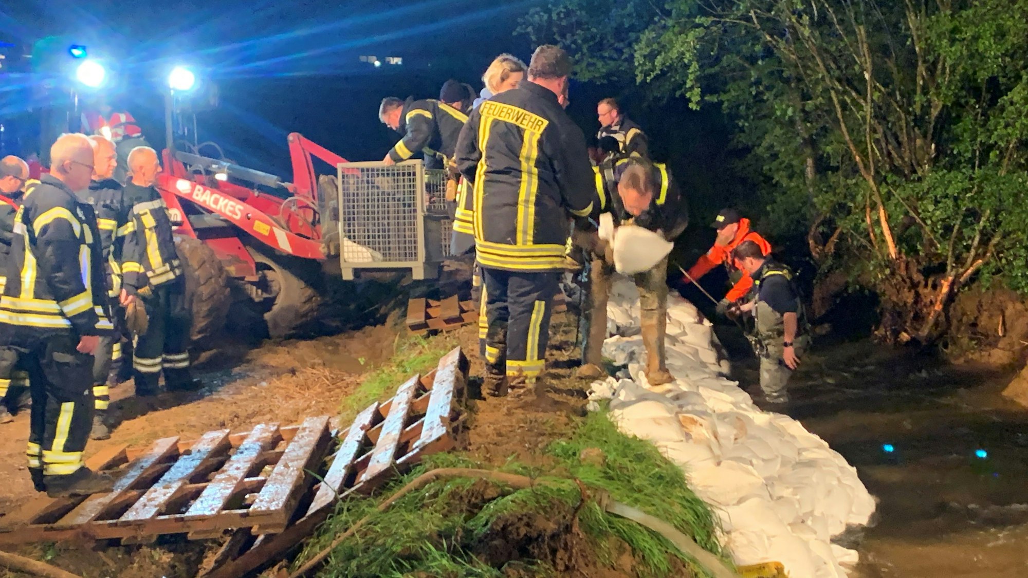 Einsatzkräfte des THW und der Feuerwehr befestigen mit Sandsäcken einen aufgeschütteten Damm.