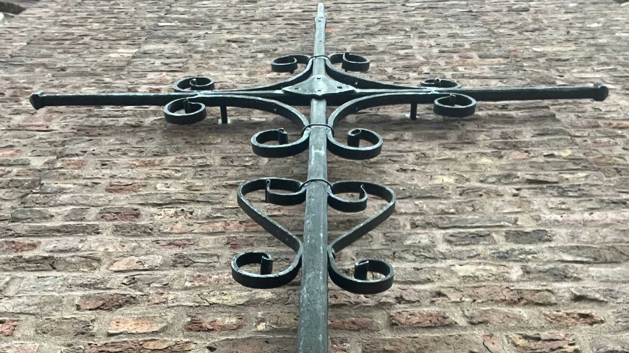 Zu sehen ist ein Kreuz aus Metall an der Außenmauer der Kirche.