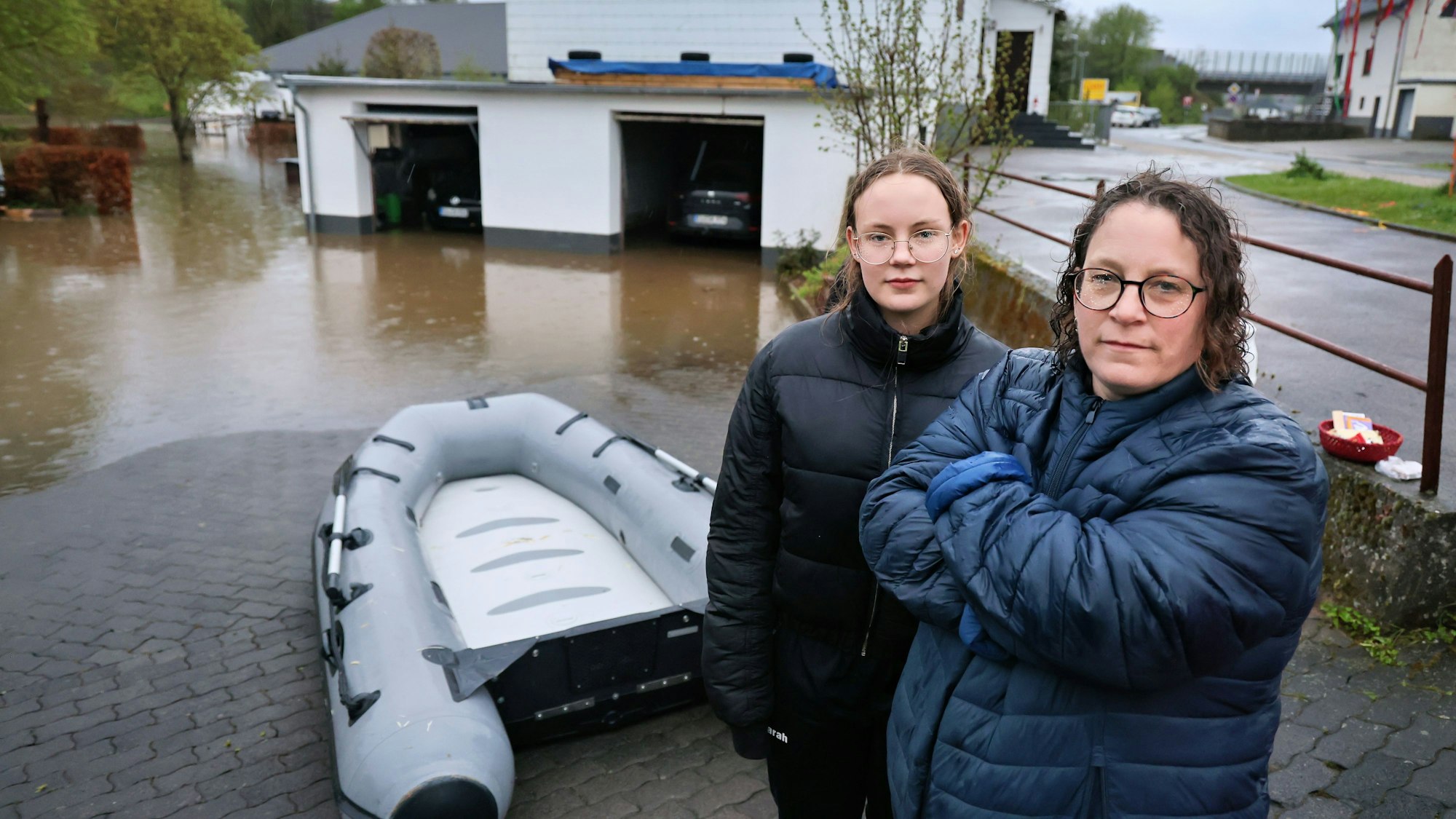 Silke Klimpel und ihre Tochter stehen vor dem Schlauchboot. Das Grundstück ist überschwemmt. In die Garagen, in denen zwei Autos stehen, ist das Wasser eingedrungen.