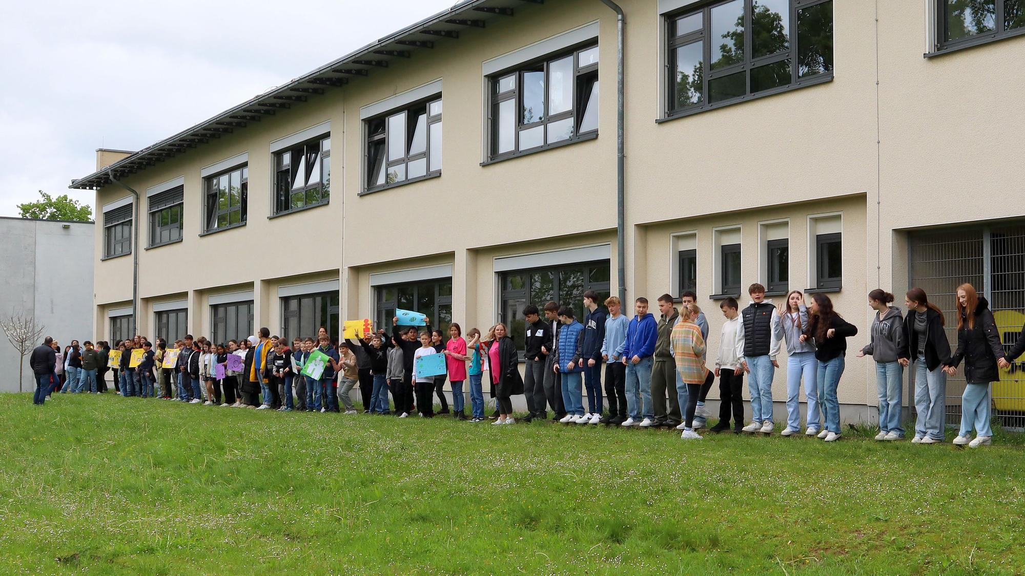 Schülerinnen und Schüler, Lehrkräfte sowie Niederkasseler Bürgerinnen und Bürger haben mit einer Menschenkette um die Alfred-Delp-Realschule Demokratie, Menschenrechte und Vielfalt demonstriert.