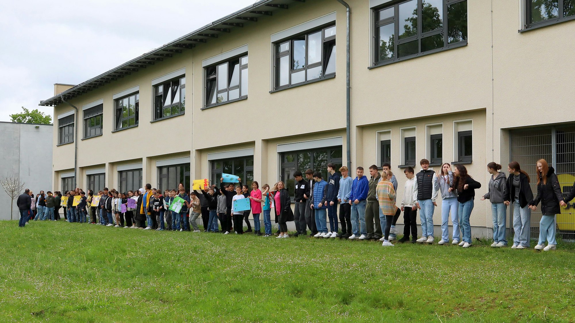 Schülerinnen und Schüler, Lehrkräfte sowie Niederkasseler Bürgerinnen und Bürger haben mit einer Menschenkette um die Alfred-Delp-Realschule Demokratie, Menschenrechte und Vielfalt demonstriert.