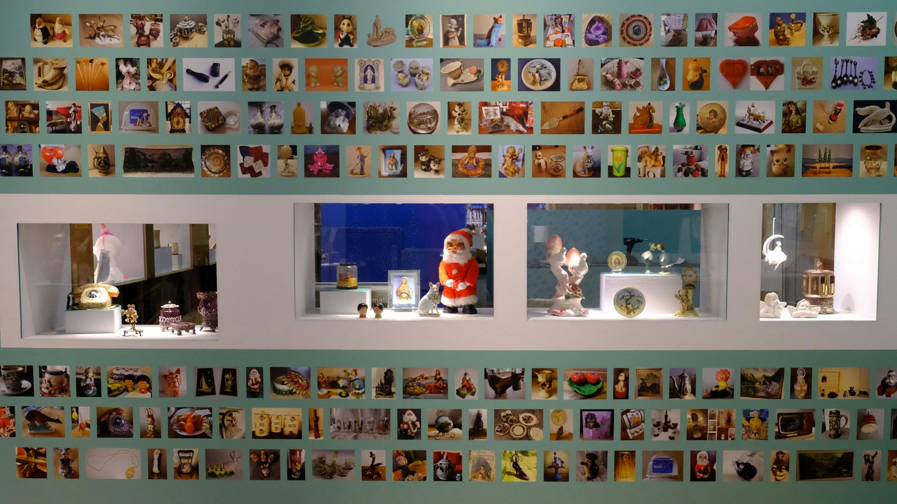 Eine Ausstellungswand mit vier Schaukästen darüber und darunter hängen zahlreiche Fotos weiterer Exponate.