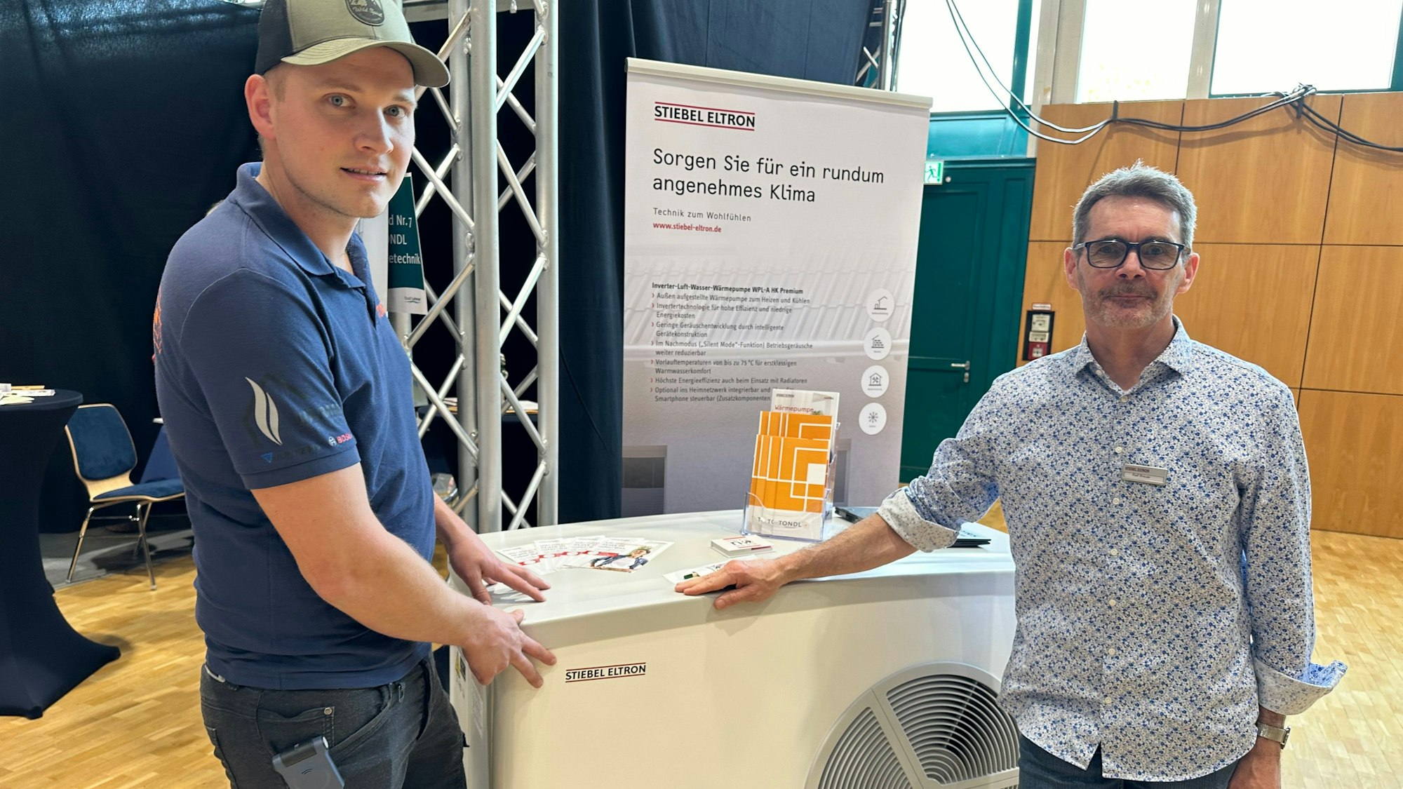 Oliver Tondl (l.) einer der beiden Geschäftsführer der gleichnamigen Firma, an einer Luftwärmepumpe auf der Nachhaltigkeits- und Mobilitätsmesse in Lohmar.