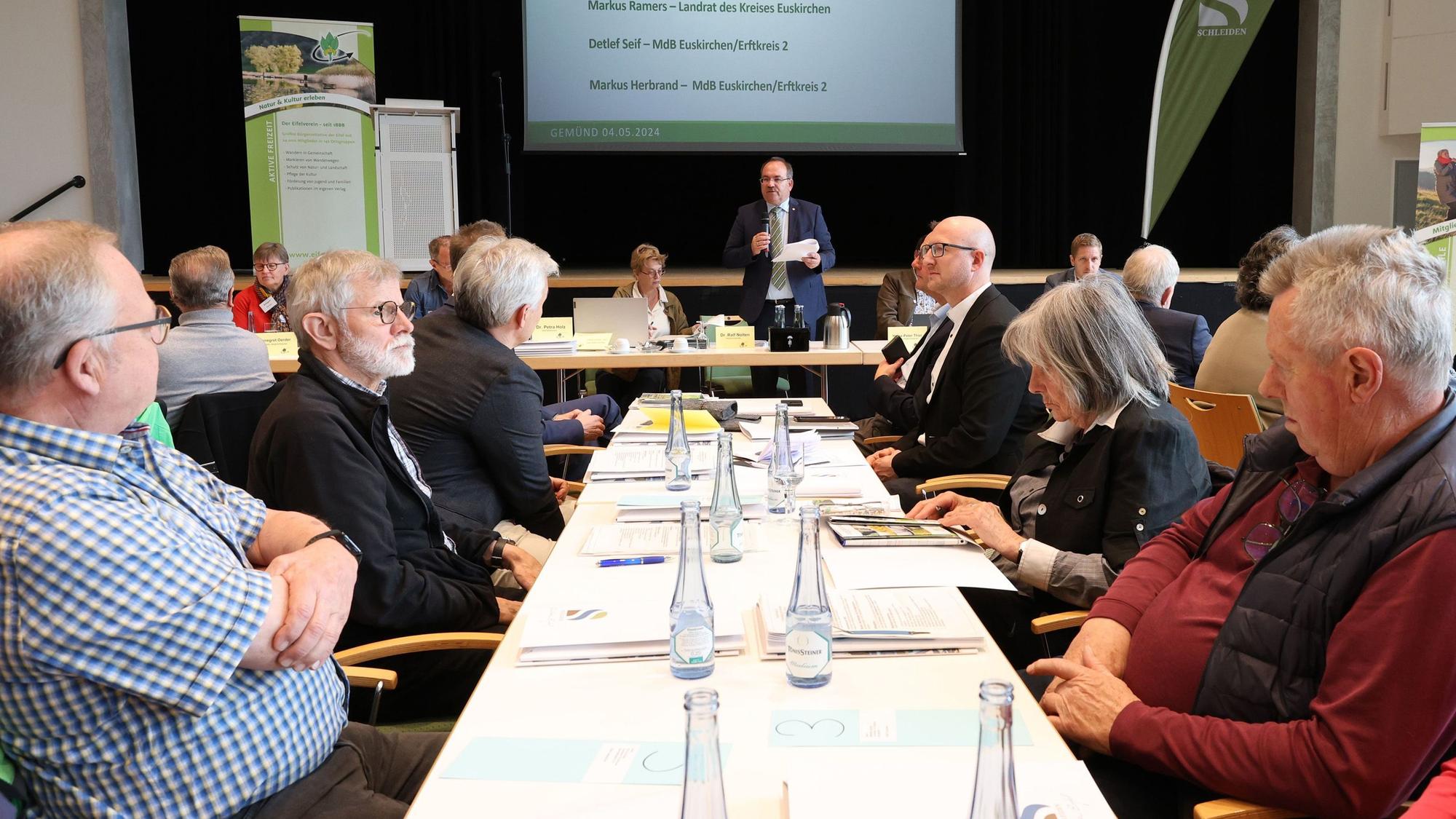 Zahlreiche Personen sitzen bei der Tagung des Eifelvereins im Kursaal Gemünd an Tischen. In der Mitte steht Hauptvorsitzender Dr. Ralf Nolten.