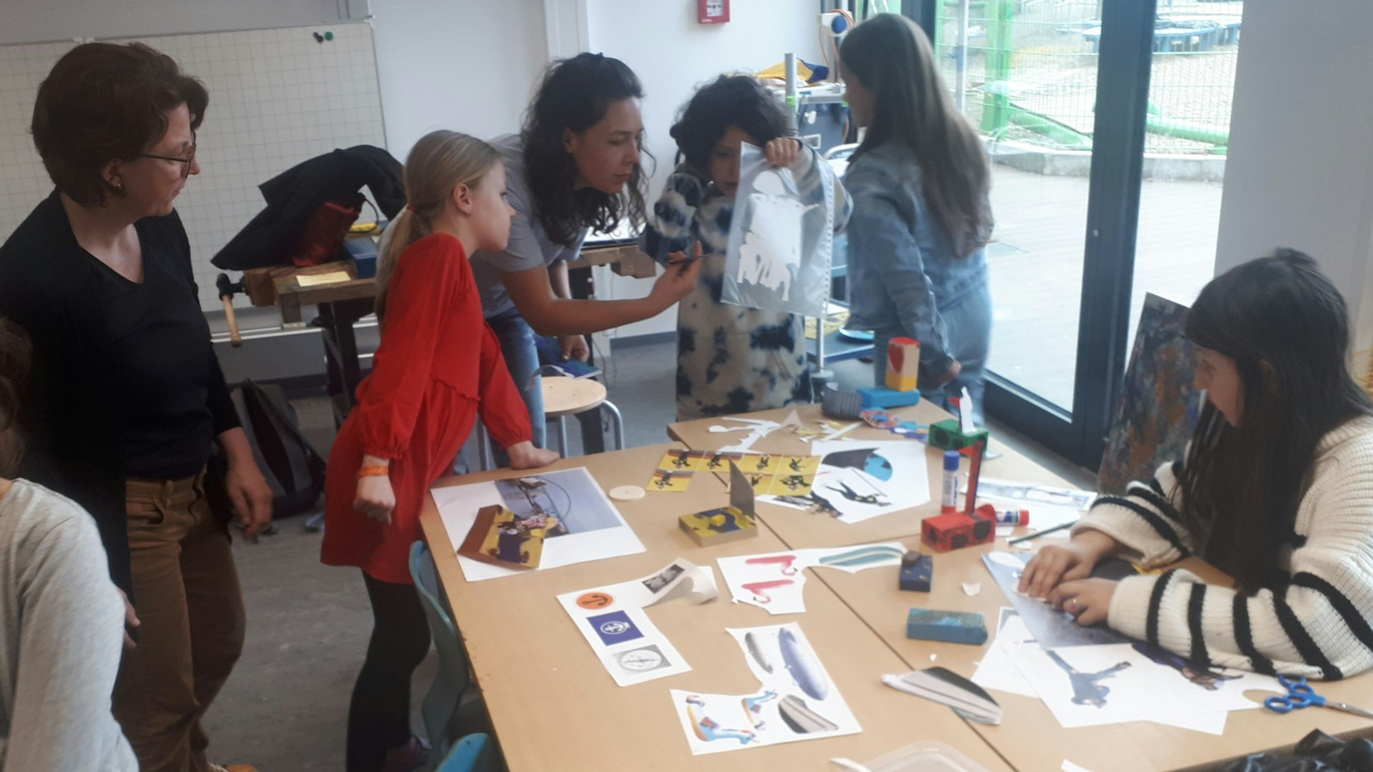 Schülerinnen und Schüler sowie Lehrerinnen stehen an einem Tisch in der Grundschule GGS Halfengasse. Sie beteiligten sich an dem Kunstprojekt des Vereins Fährkultur Köln-Nord. Foto von Bernd Schöneck