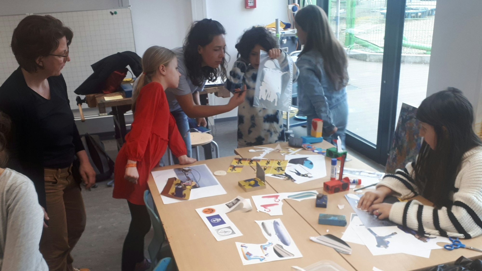 Schülerinnen und Schüler sowie Lehrerinnen stehen an einem Tisch in der Grundschule GGS Halfengasse. Sie beteiligten sich an dem Kunstprojekt des Vereins Fährkultur Köln-Nord. Foto von Bernd Schöneck