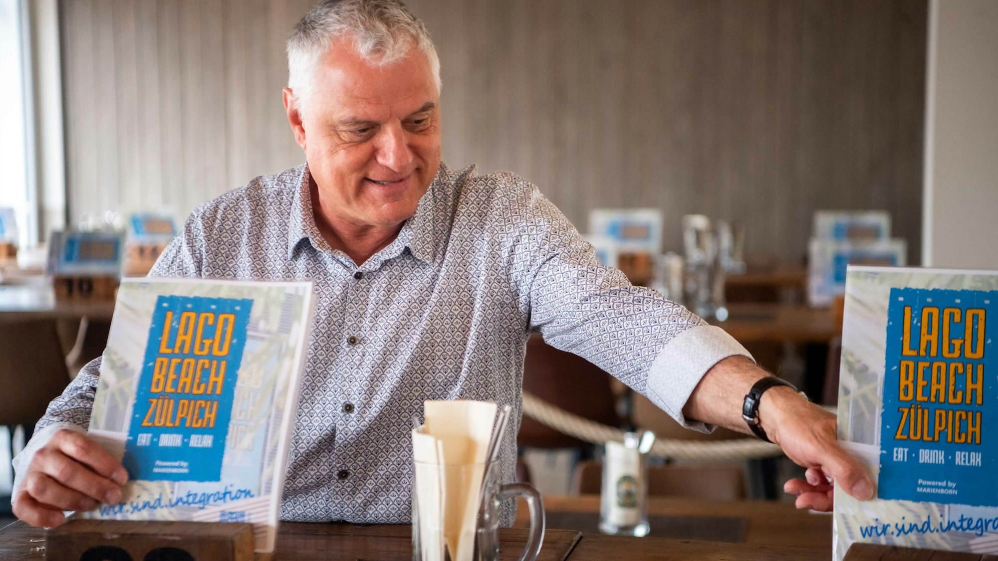 Das Bild zeigt den Eventmanager, wie er die Speisekarten auf den Tisch stellt.