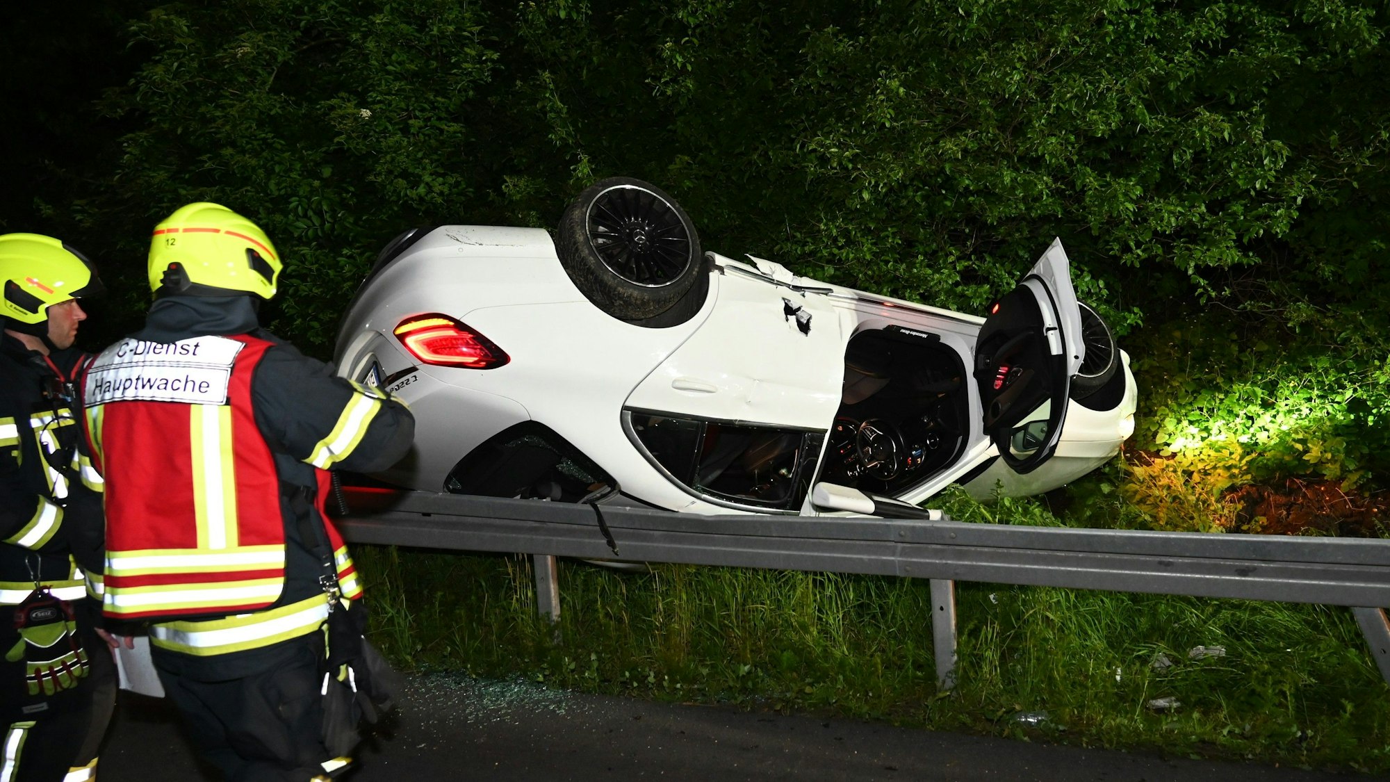 Auf dem Foto ist ein weißes Auto zu sehen, das hinter der Leitplanke auf dem Grünstreifen auf dem Dach liegt.