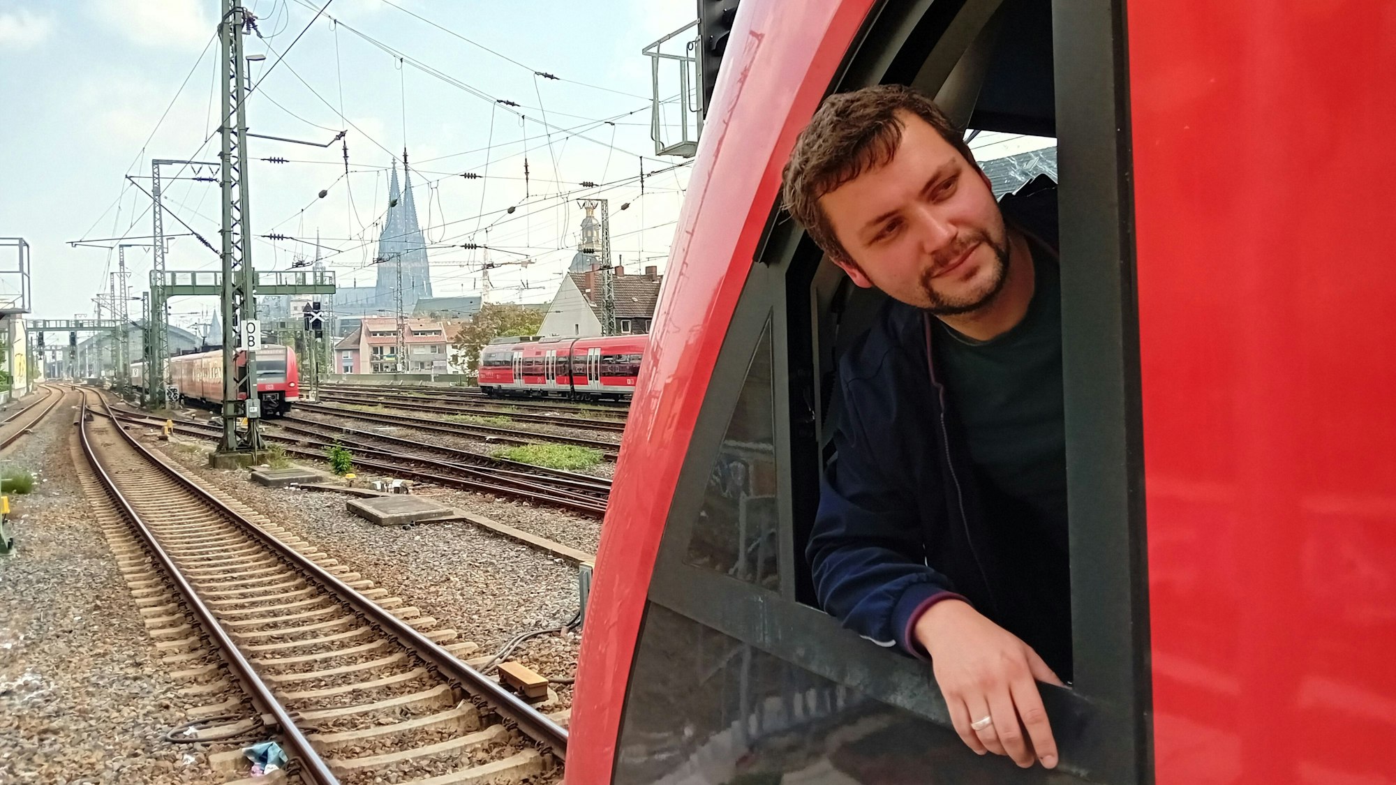 Der Lokführer lehnt aus dem Fenster, im Hintergrund sieht man den Dom.