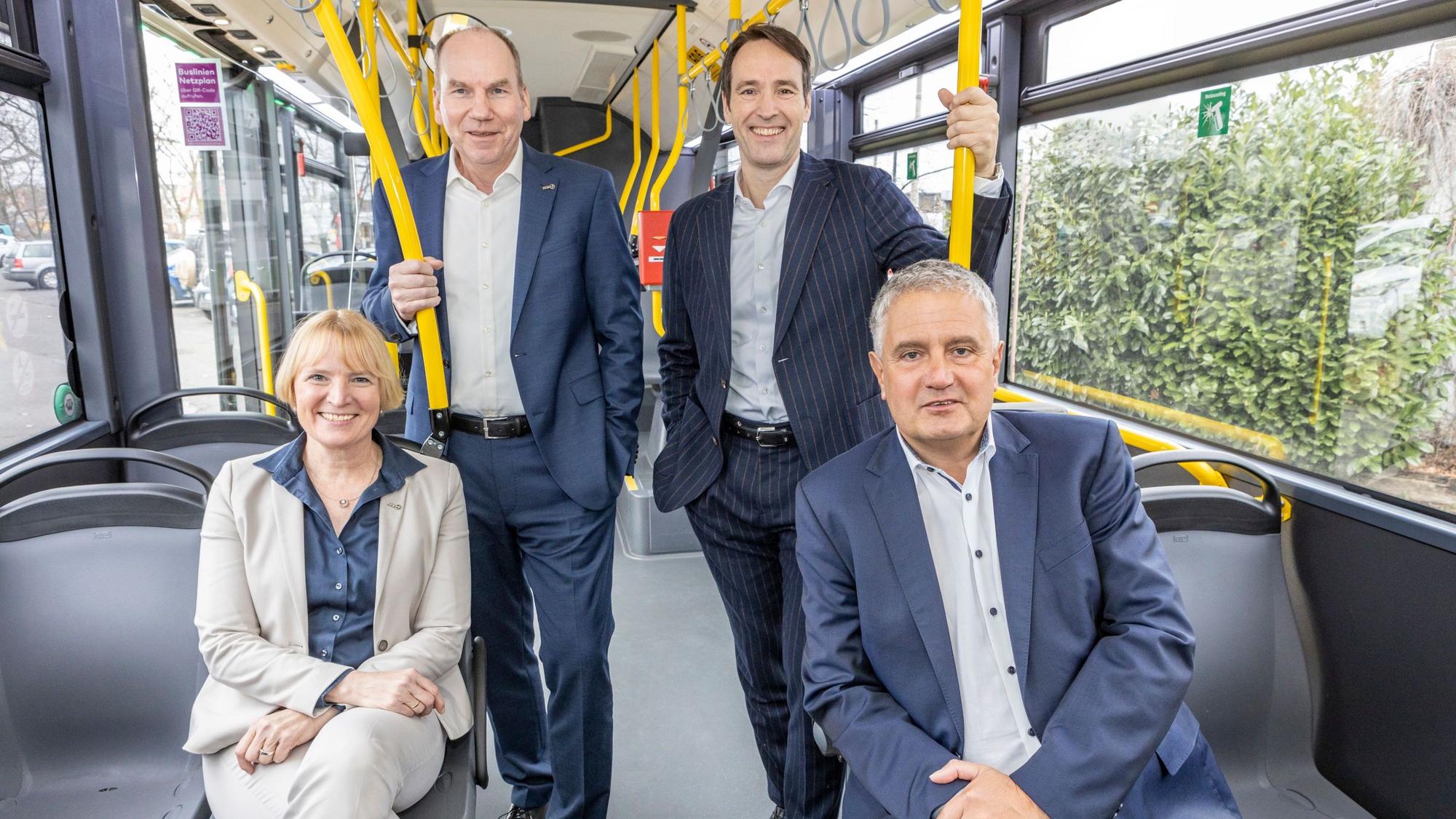 Drei Männer und eine Frau stehen, bzw. sitzen in einem Bus.