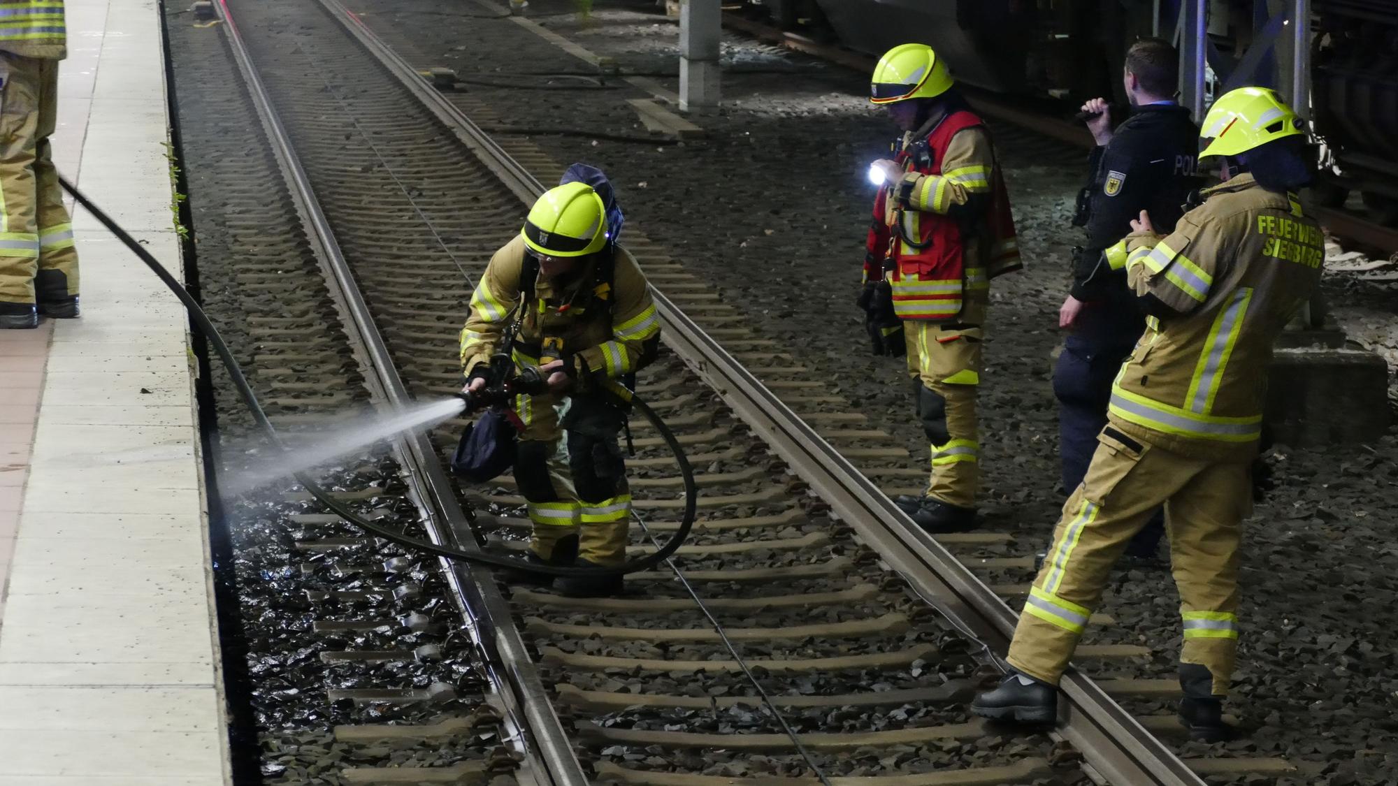 Feuerwehrleute stehen auf Schienen.