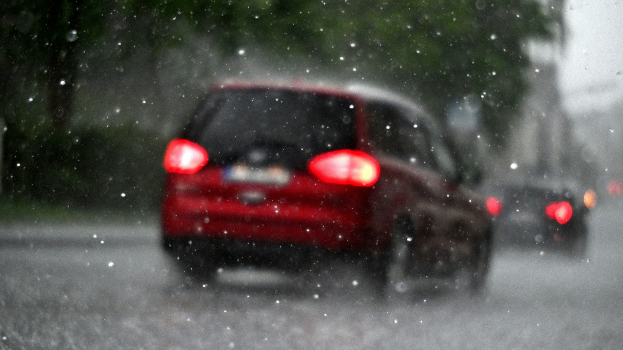 Ein Auto fährt durch einen Hagelschauer. Der DWD warnt vor Starkregen in Köln und der Region. (Symbolbild)