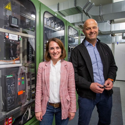 Eine Frau und ein Mann stehen vor einem Schaltschrank.