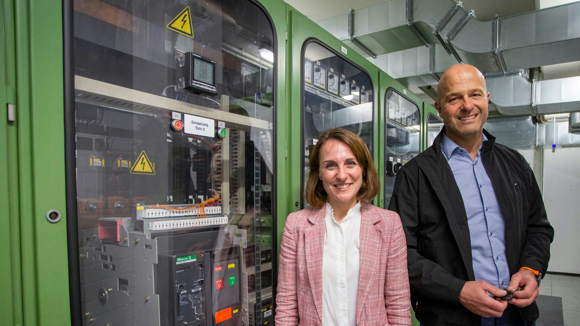 Eine Frau und ein Mann stehen vor einem Schaltschrank.