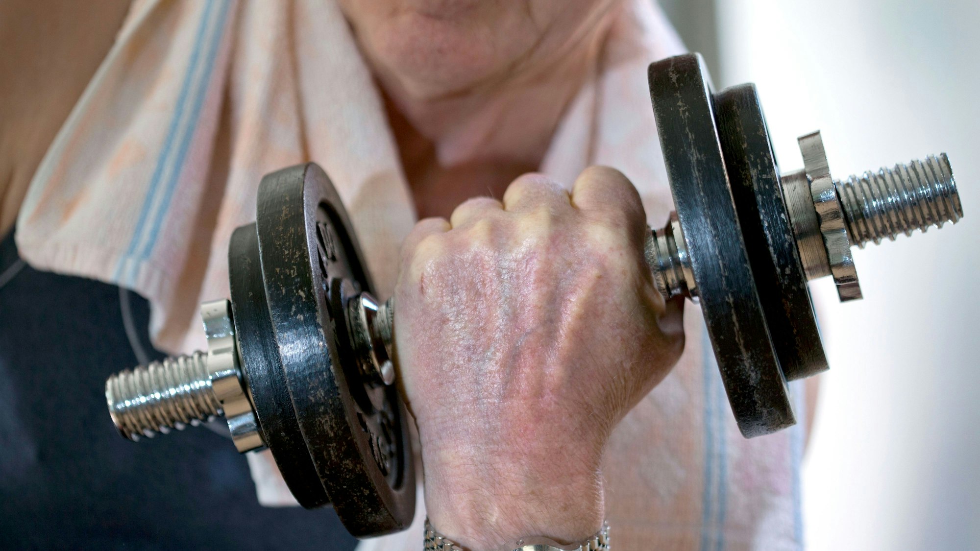 Das Foto zeigt einen älteren Menschen, der eine Hantel stemmt.