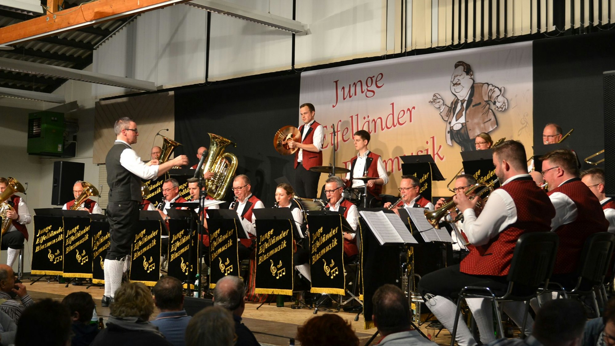 Die jungen Eifelländer Blasmusiker sitzen auf einer Bühne und geben ein Konzert.