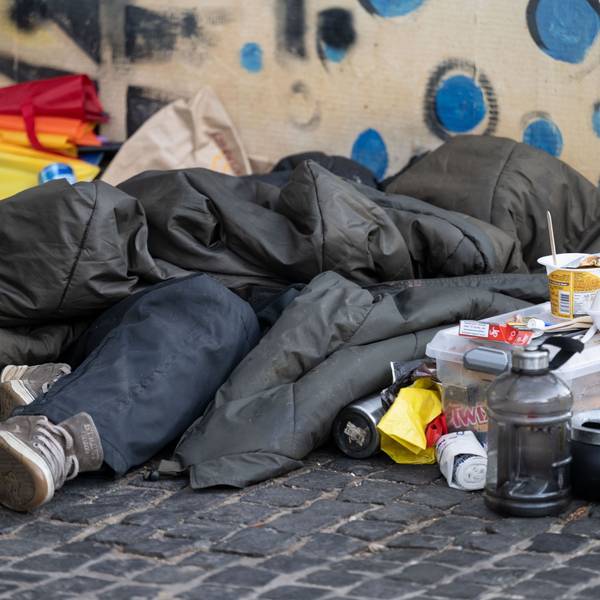 Eine Person liegt in der Innenstadt unter einem Schlafsack.